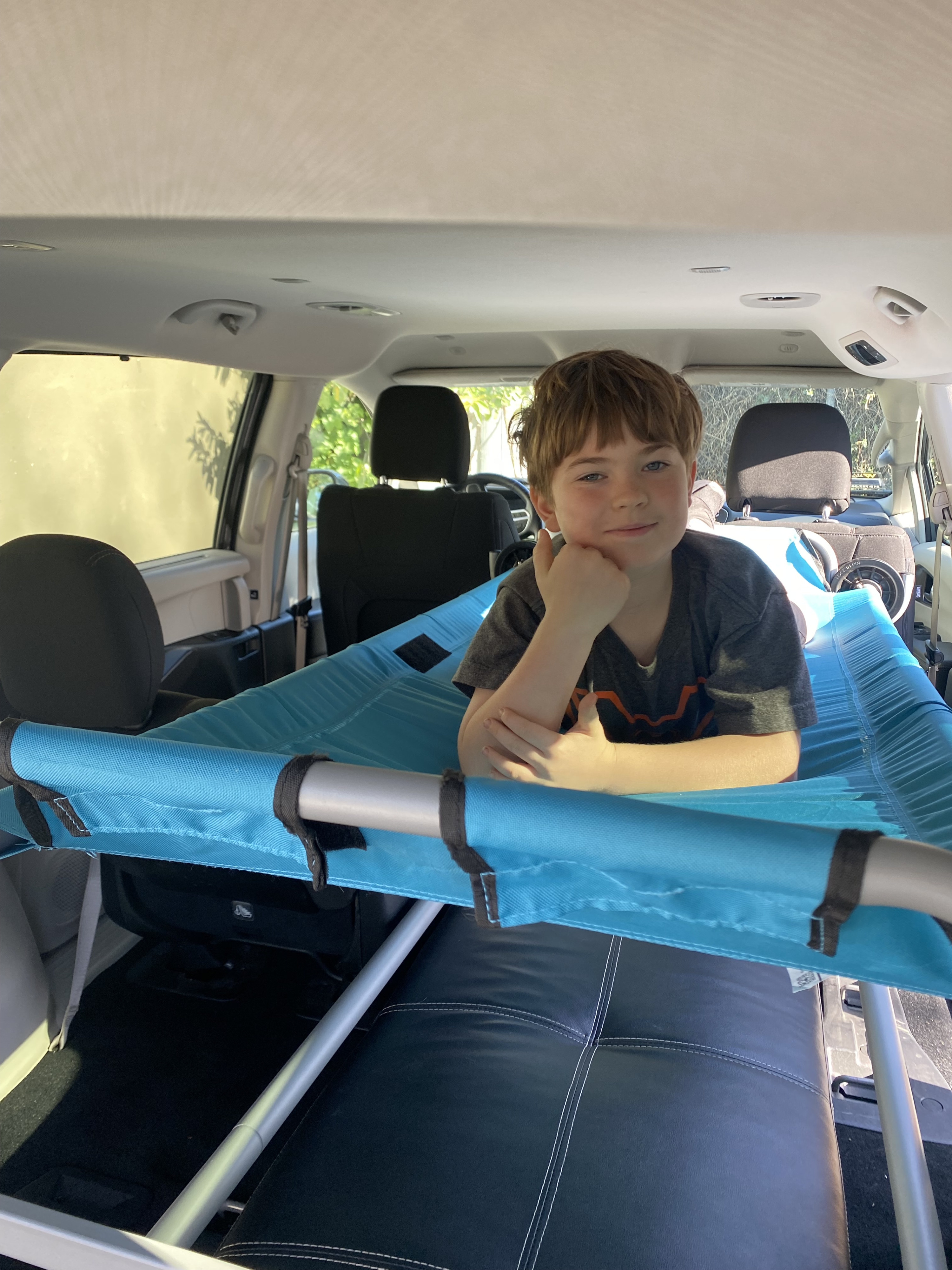 Young boy on a custom turquoise cot inside an RV rental. A comfy setup for travel adventures!. Chrysler Pacifica 2022