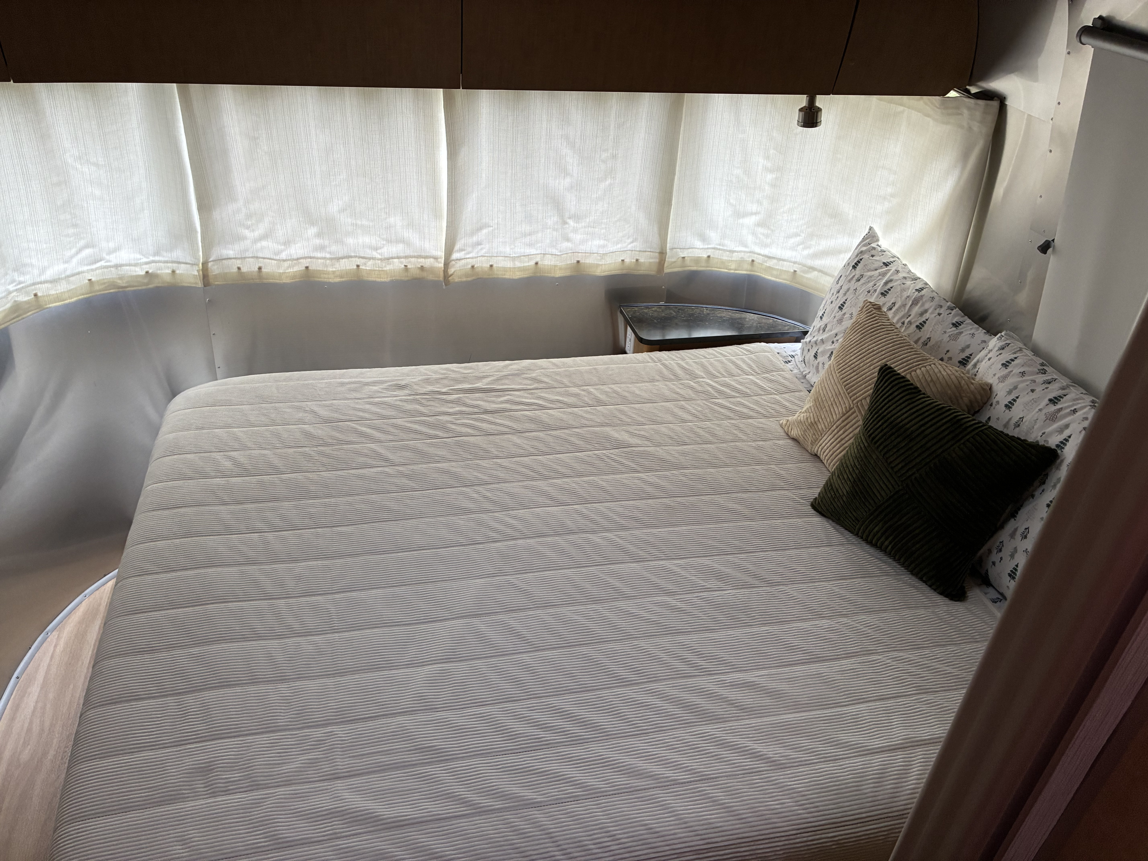 Cozy RV rental bedroom with striped bed, throw pillows, and curved walls.. Airstream Flying Cloud 2012