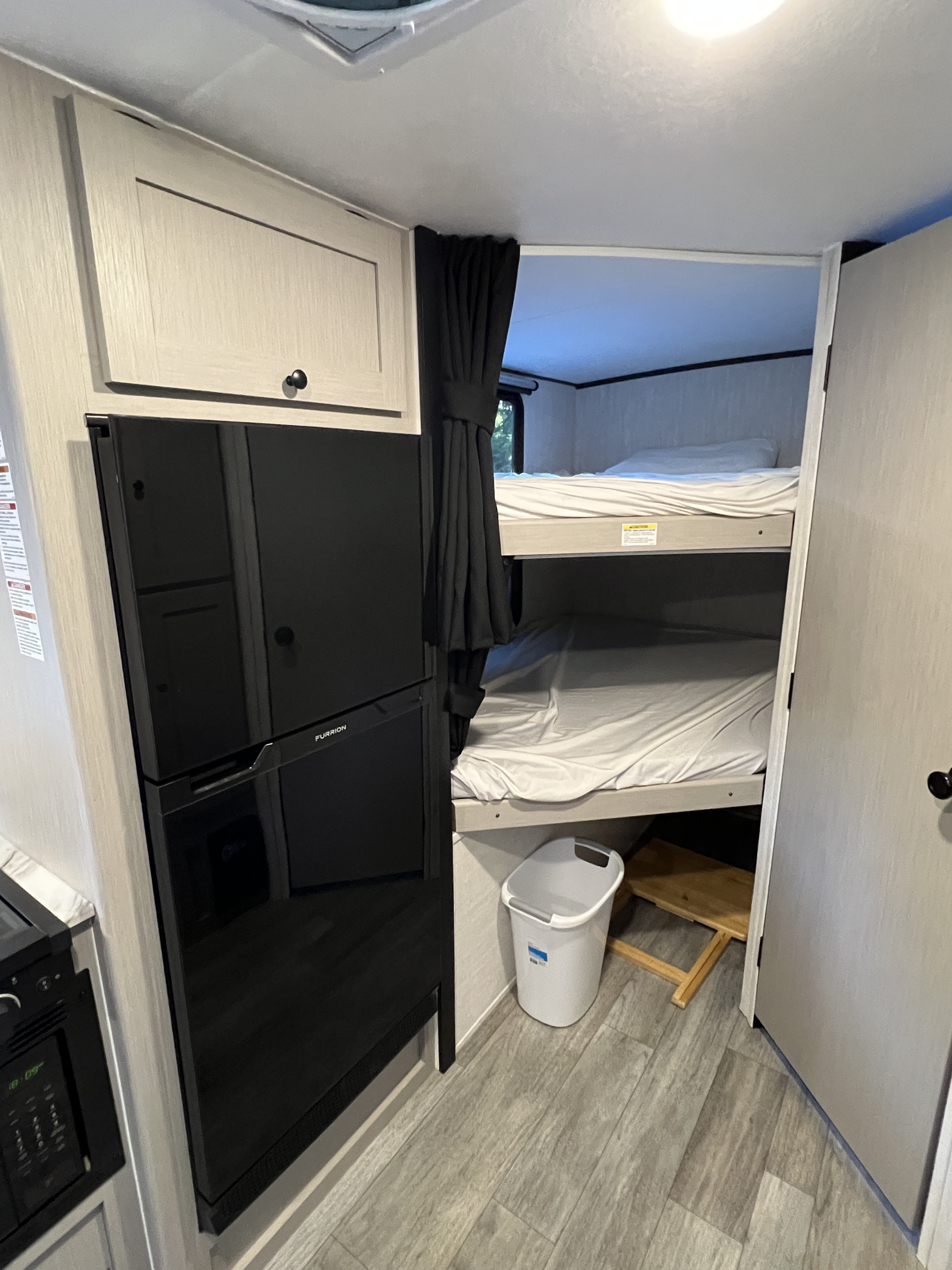 RV rental interior: modern fridge, compact kitchen, and cozy bunk beds with privacy curtain. Perfect for family adventures.. Coachmen Apex 2026