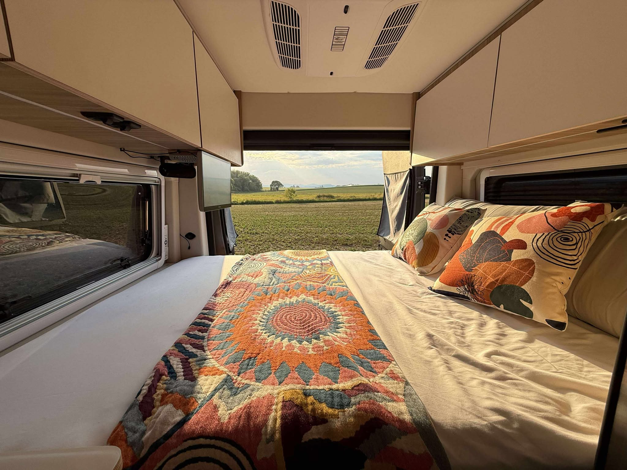 Inside a comfy **RV rental**: A bed with a colorful blanket faces a peaceful field and sky view.. Coachmen PIXEL 2026
