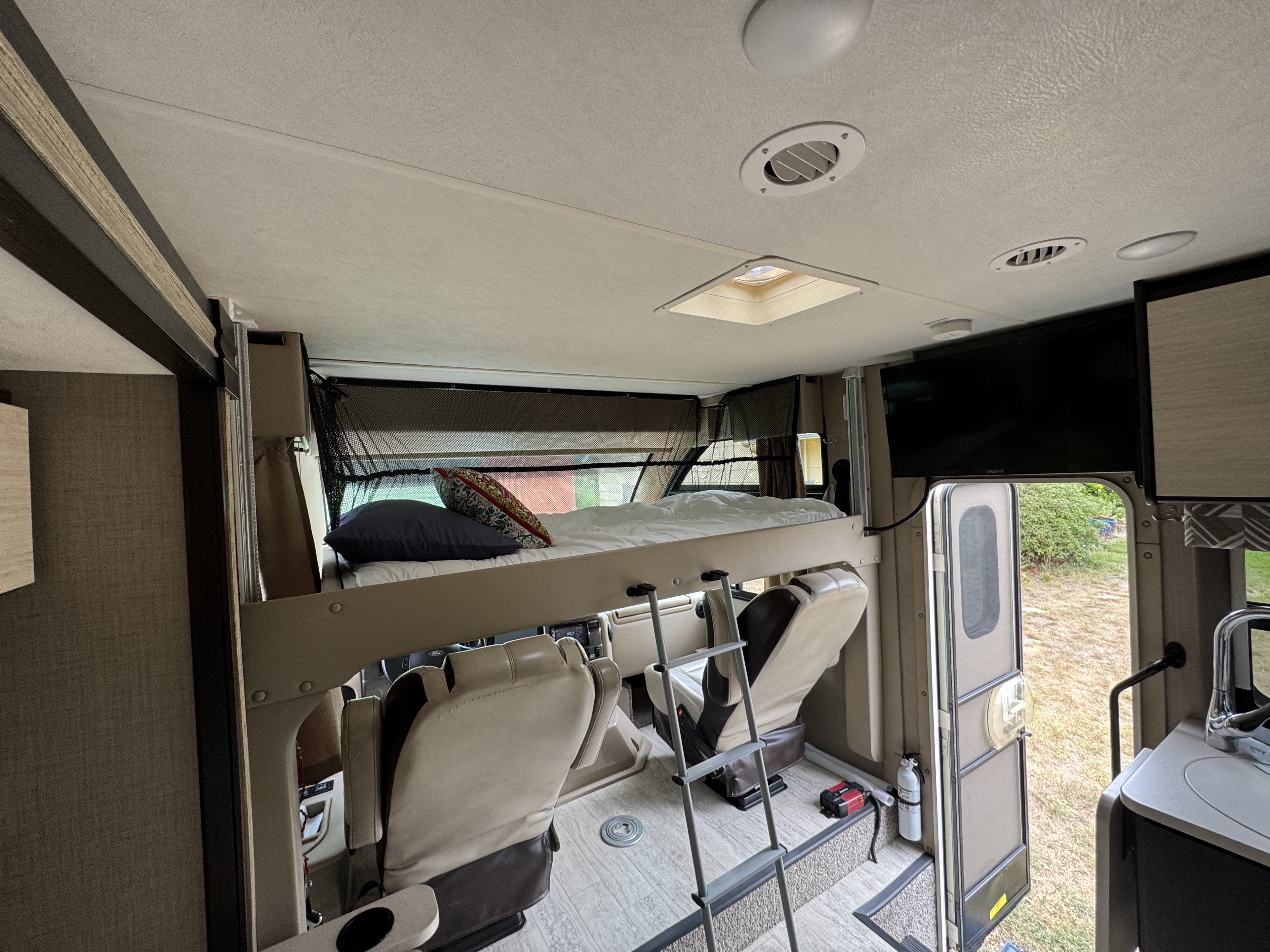 RV rental interior: over-cab bunk bed with ladder, cockpit, and basic kitchen. Ideal for camping trips.. Thor Axis 2020