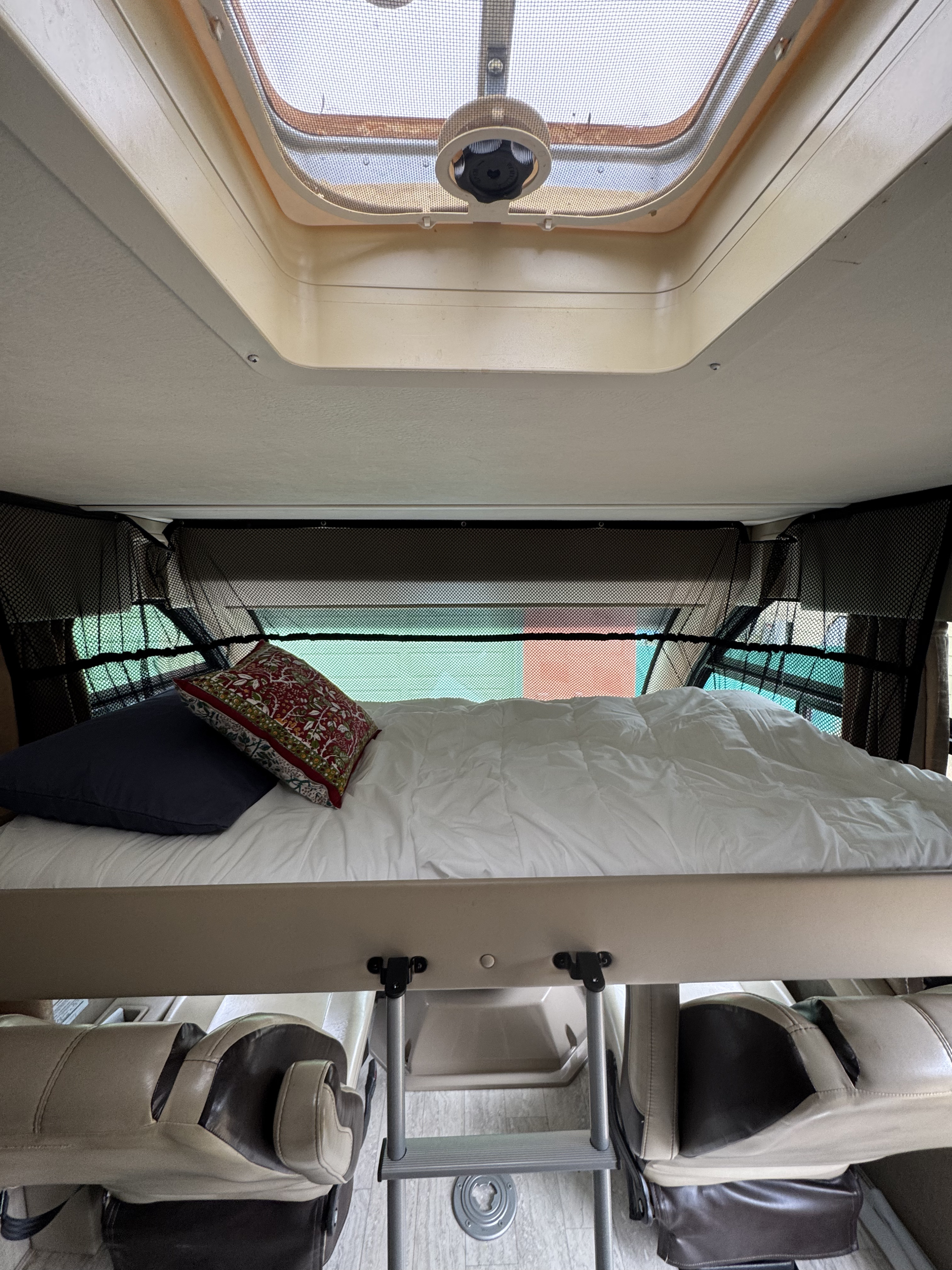 Cozy overhead bed in an RV rental, featuring skylight, safety net, and ladder access.. Thor Axis 2020