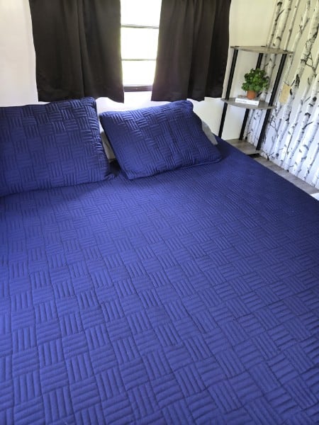 This RV rental's cozy bedroom features a royal blue quilted bed, matching pillows, and a small decorative shelf.. Coachmen Leprechaun 2001