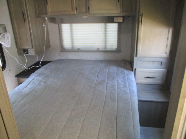 Inside an RV rental: a light-colored bedroom with a large bed, window, overhead cabinets, and built-in storage.. Coachmen Freelander 27QB 2021