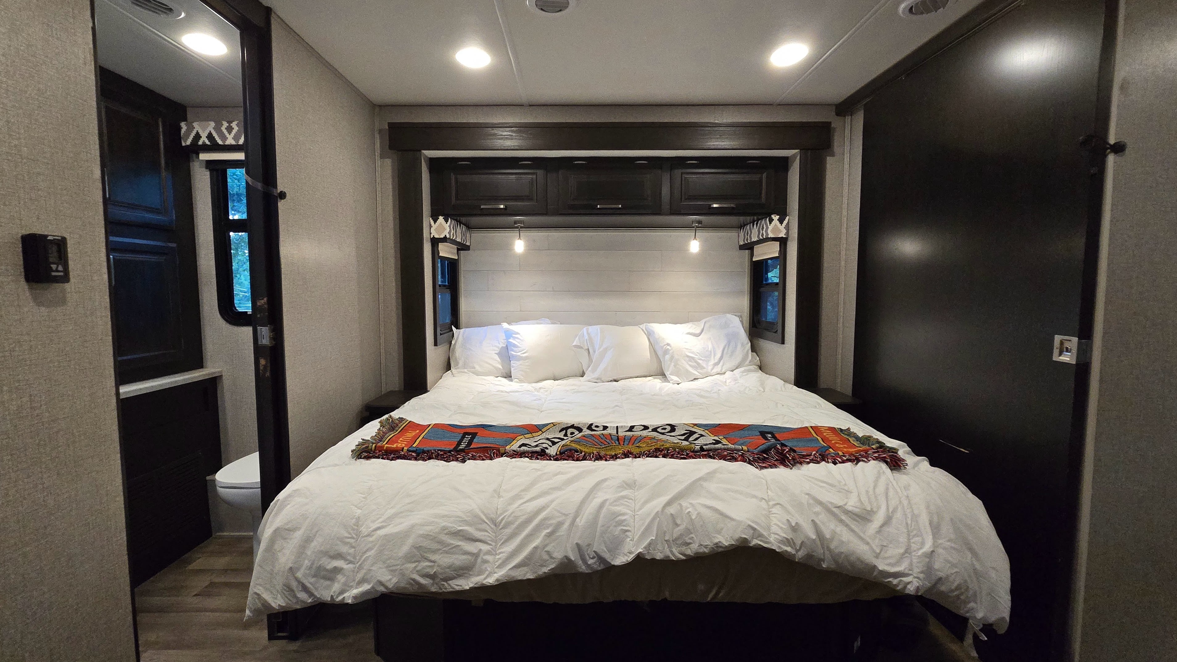 Bright & cozy **RV rental** bedroom. White bed, colorful throw, storage, & bathroom access. Ideal for comfortable travel.. Entegra Coach Vision XL 2021