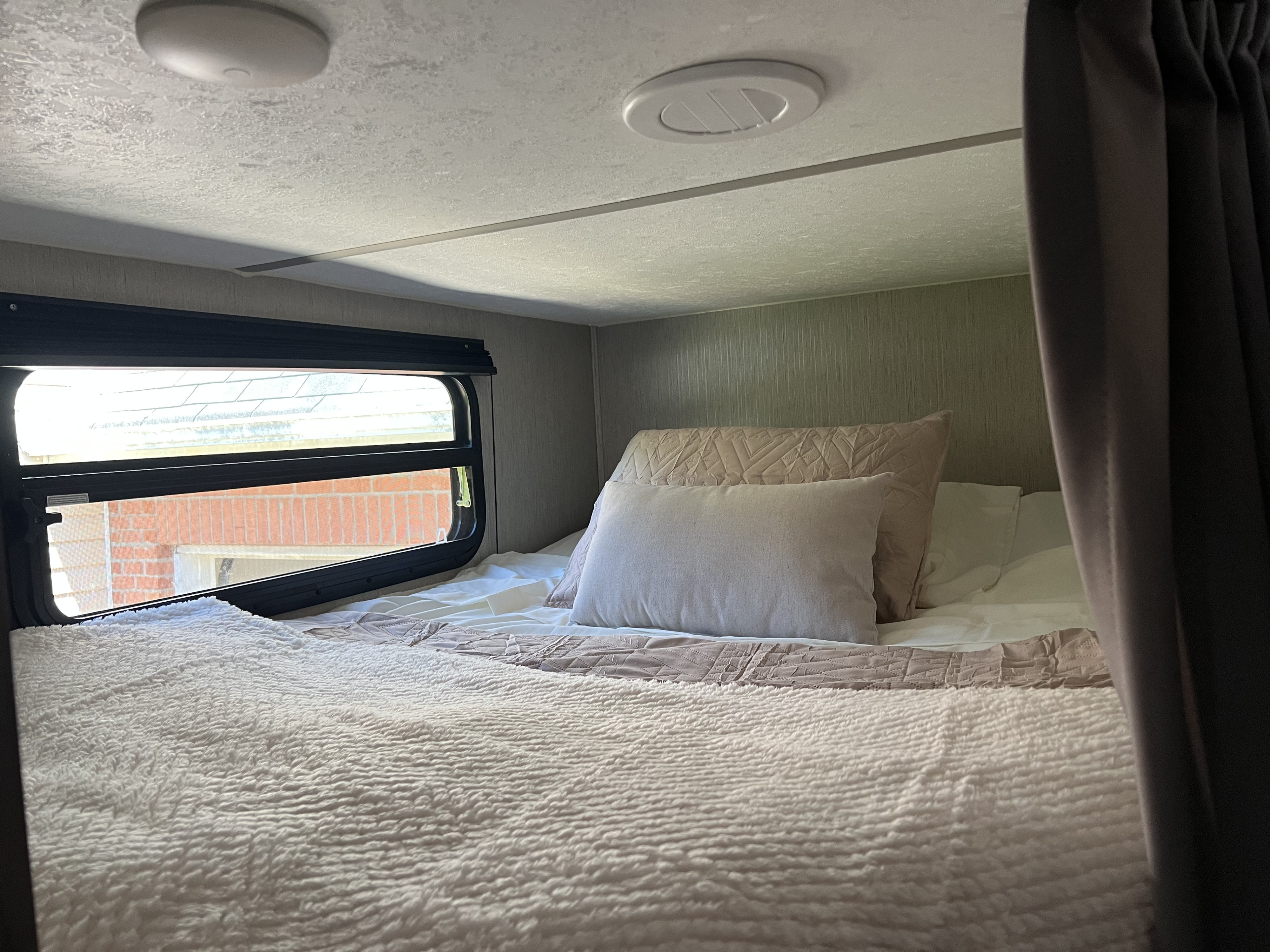 A cozy RV rental bedroom: plush bed with pillows, window showing an outdoor view, and ceiling vents/lights.. Coachmen FREEDOM EXPRESS 2021