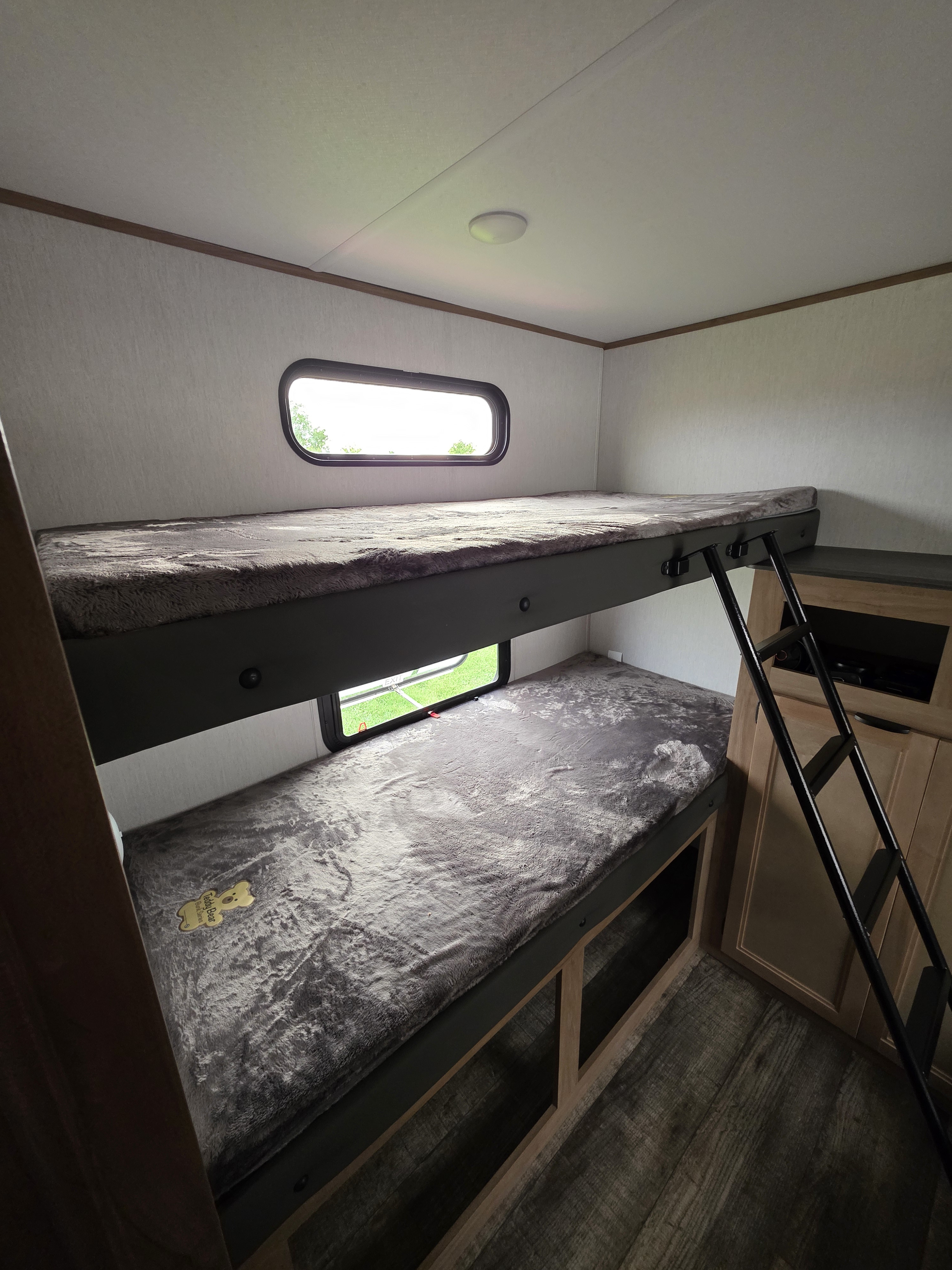 An rv rental interior featuring comfortable bunk beds with fuzzy grey blankets and two windows.. Forest River Alpha Wolf 280 QBS-L 2024