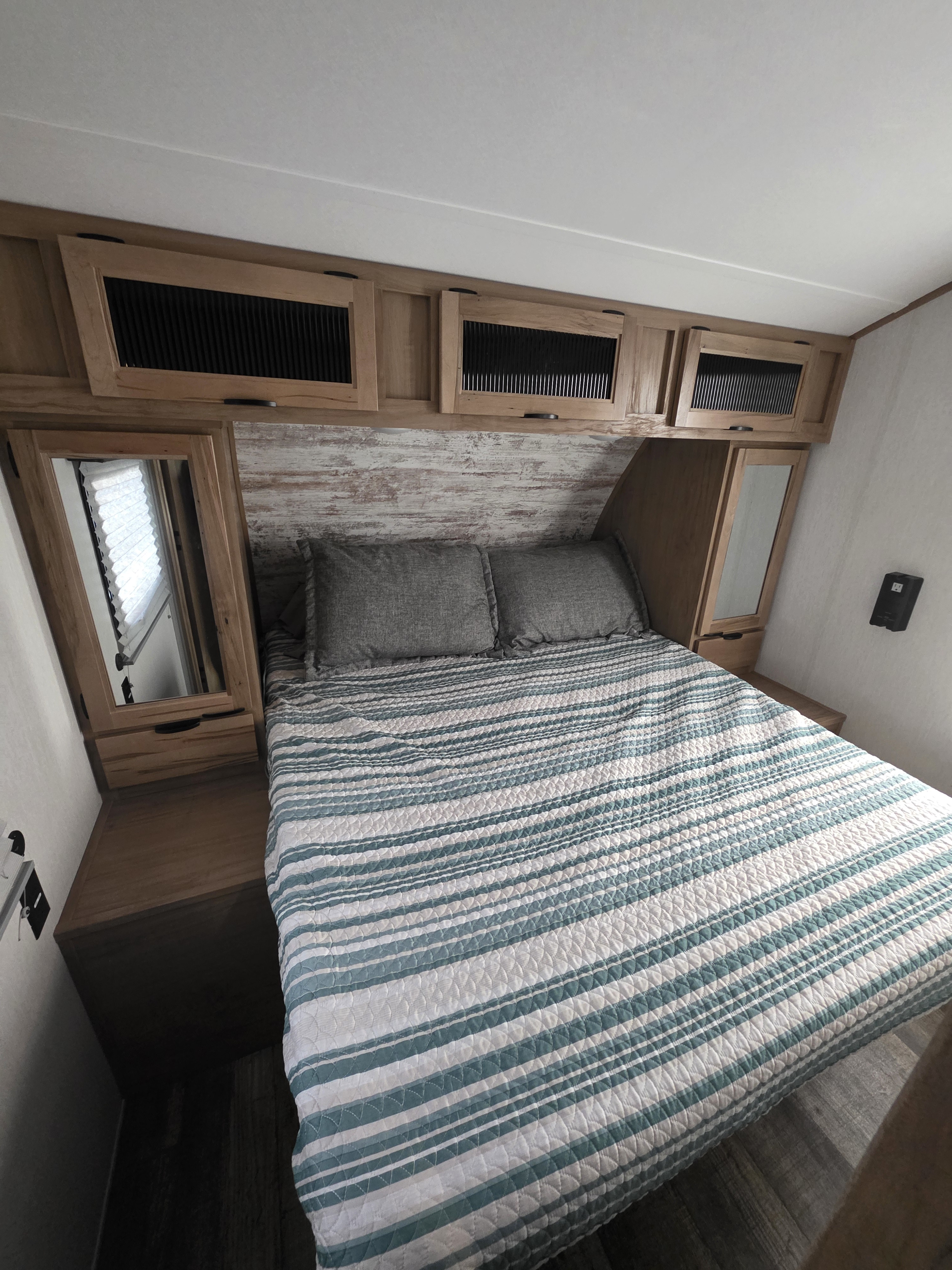 Cozy RV rental bedroom with a striped bedspread, pillows, and built-in wooden cabinets/mirrors, offering comfort for your travels.. Forest River Alpha Wolf 280 QBS-L 2024