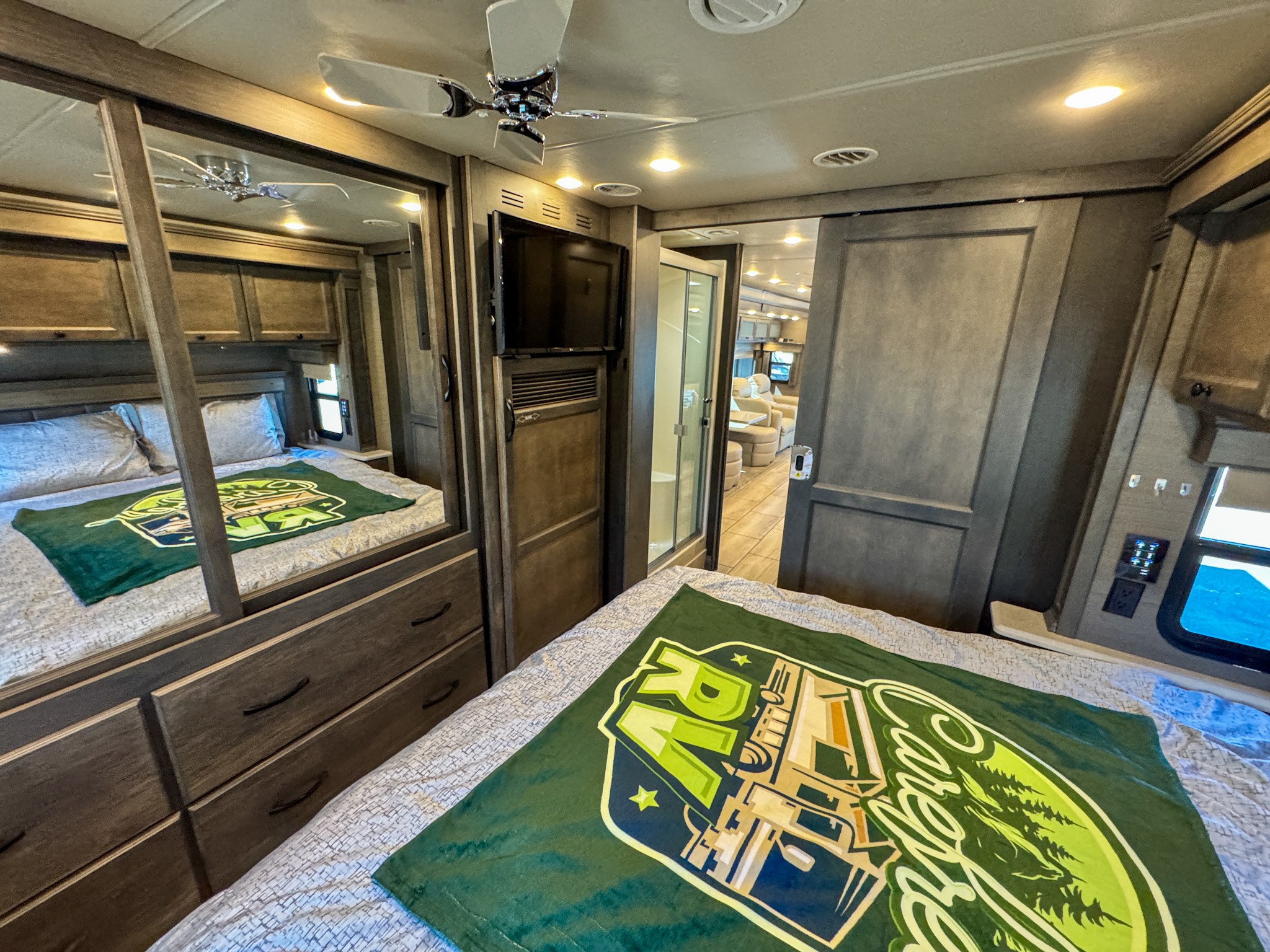Explore a spacious RV rental interior: bedroom with bed, dresser, TV, and en-suite bath access. Ideal for comfortable travel.. Tiffin Allegro Bay Super-C 2022