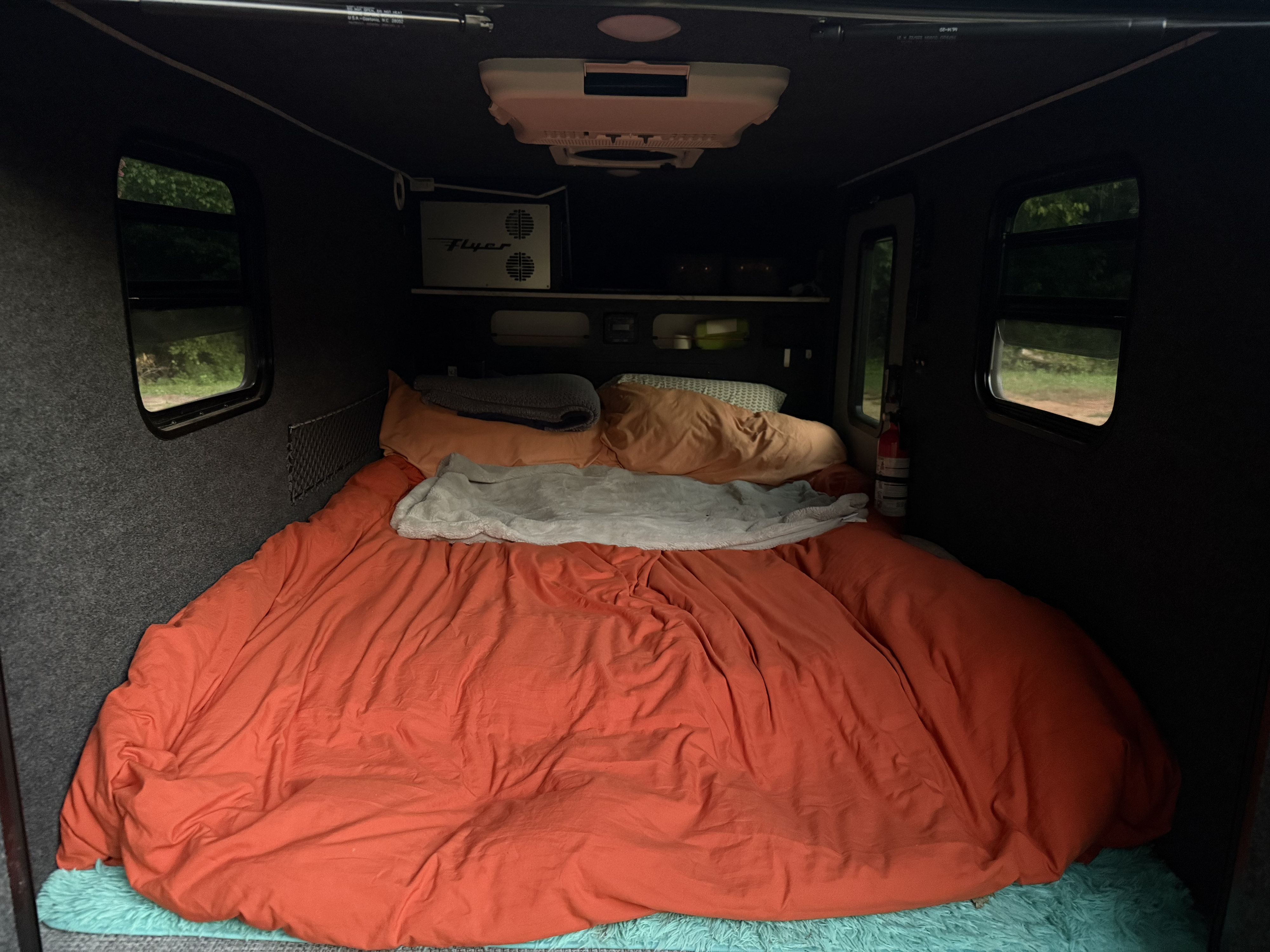 Relaxing RV rental interior with a large orange-covered bed, side windows, overhead AC, and storage.. InTech RV Flyer 2023
