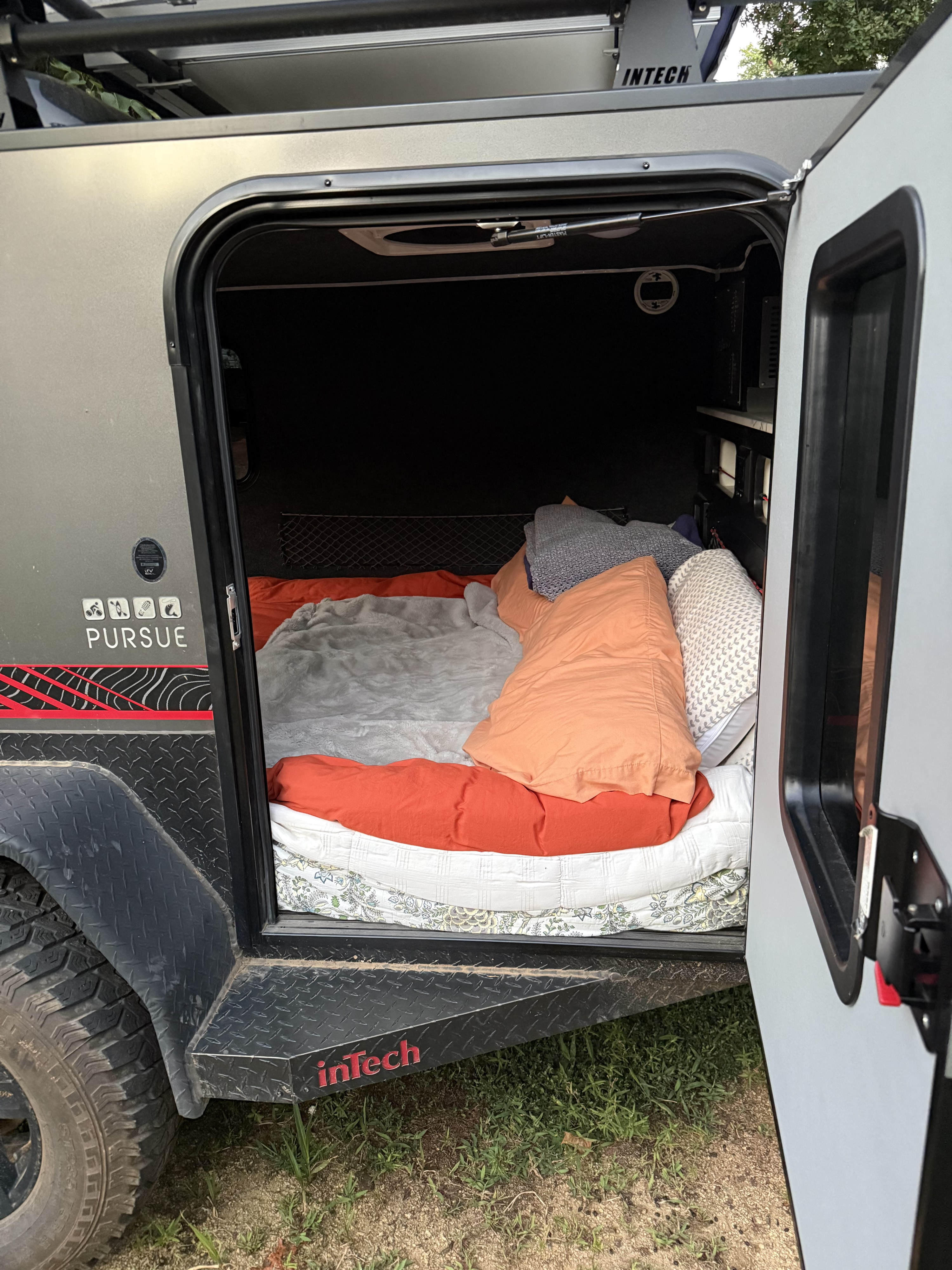 Inside an InTech Pursuit RV rental camper: a comfortable bed with orange and grey bedding seen through the open door.. InTech RV Flyer 2023