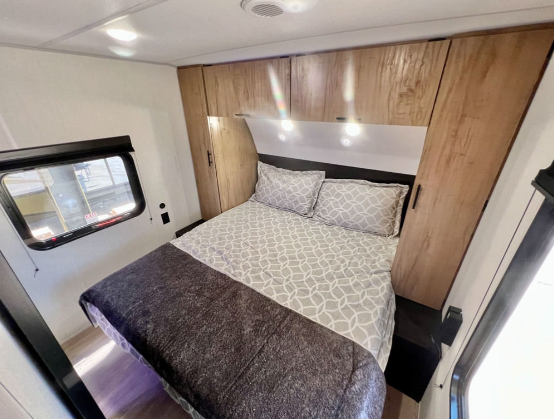 RV rental: A cozy bedroom with a large bed, wood-grain overhead cabinets, and a side window, providing comfortable travel.. Forest River Cherokee Grey Wolf 2026