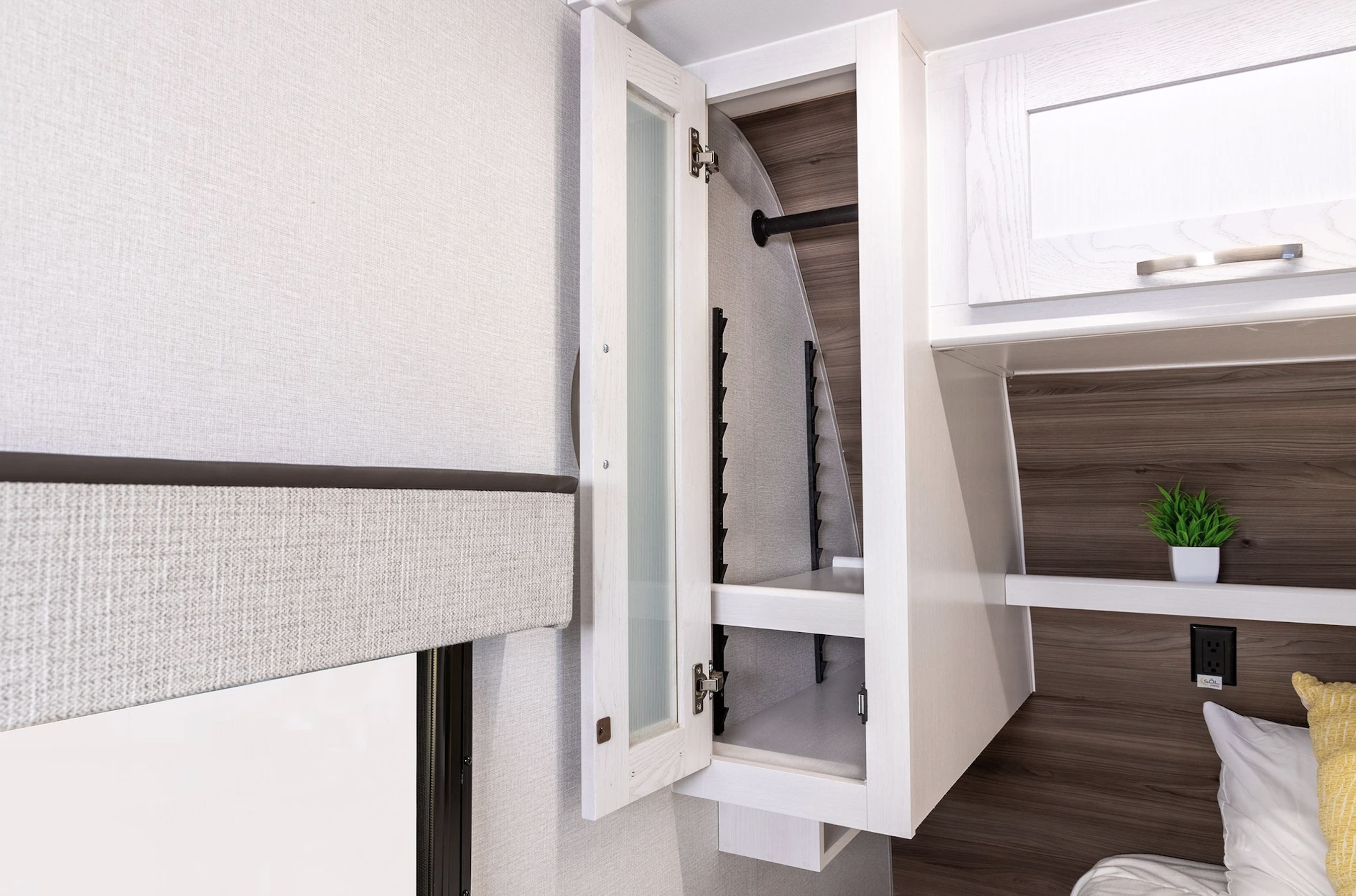 RV rental interior with an open wardrobe, window blind, and shelving, featuring a plant and outlet by the bed area.. Wayfinder RV Go Explore 2025