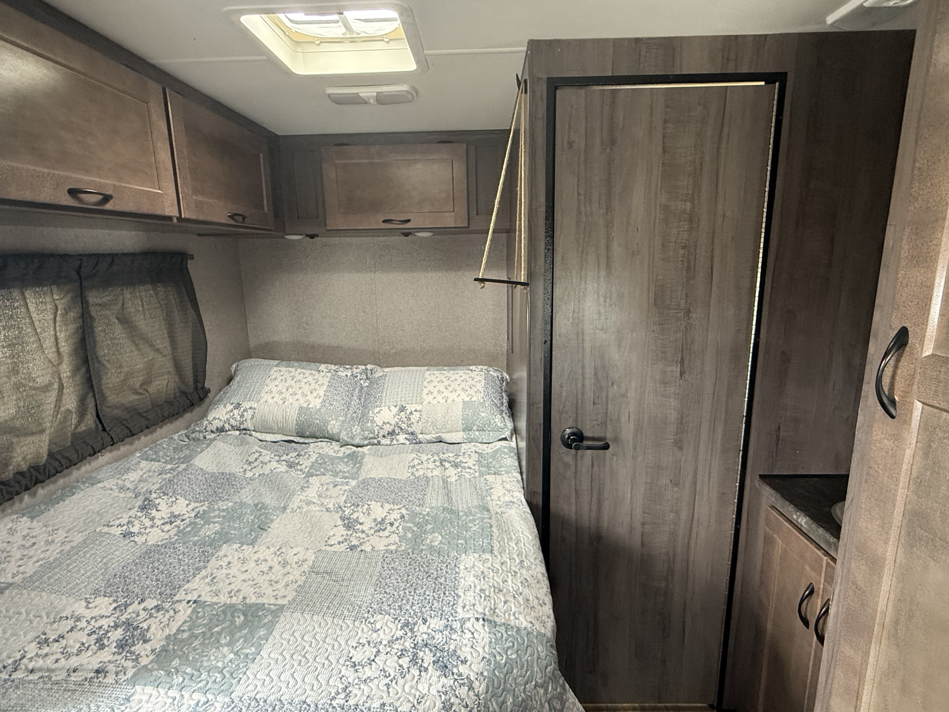RV rental: A well-appointed bedroom with a patterned bed, overhead cabinets, window, and door leading further into the unit.. Winnebago Minnie Winnie 2020