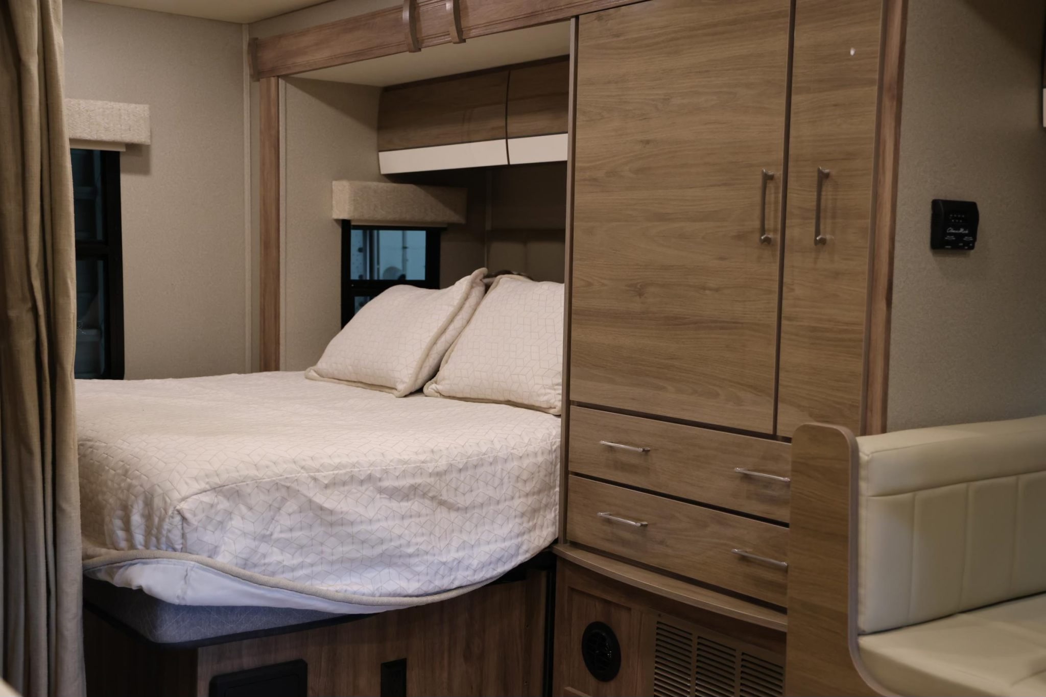 Cozy bedroom and storage in an RV rental, featuring a comfortable bed, overhead cabinets, and built-in wardrobe.. Entegra Coach Qwest 2019