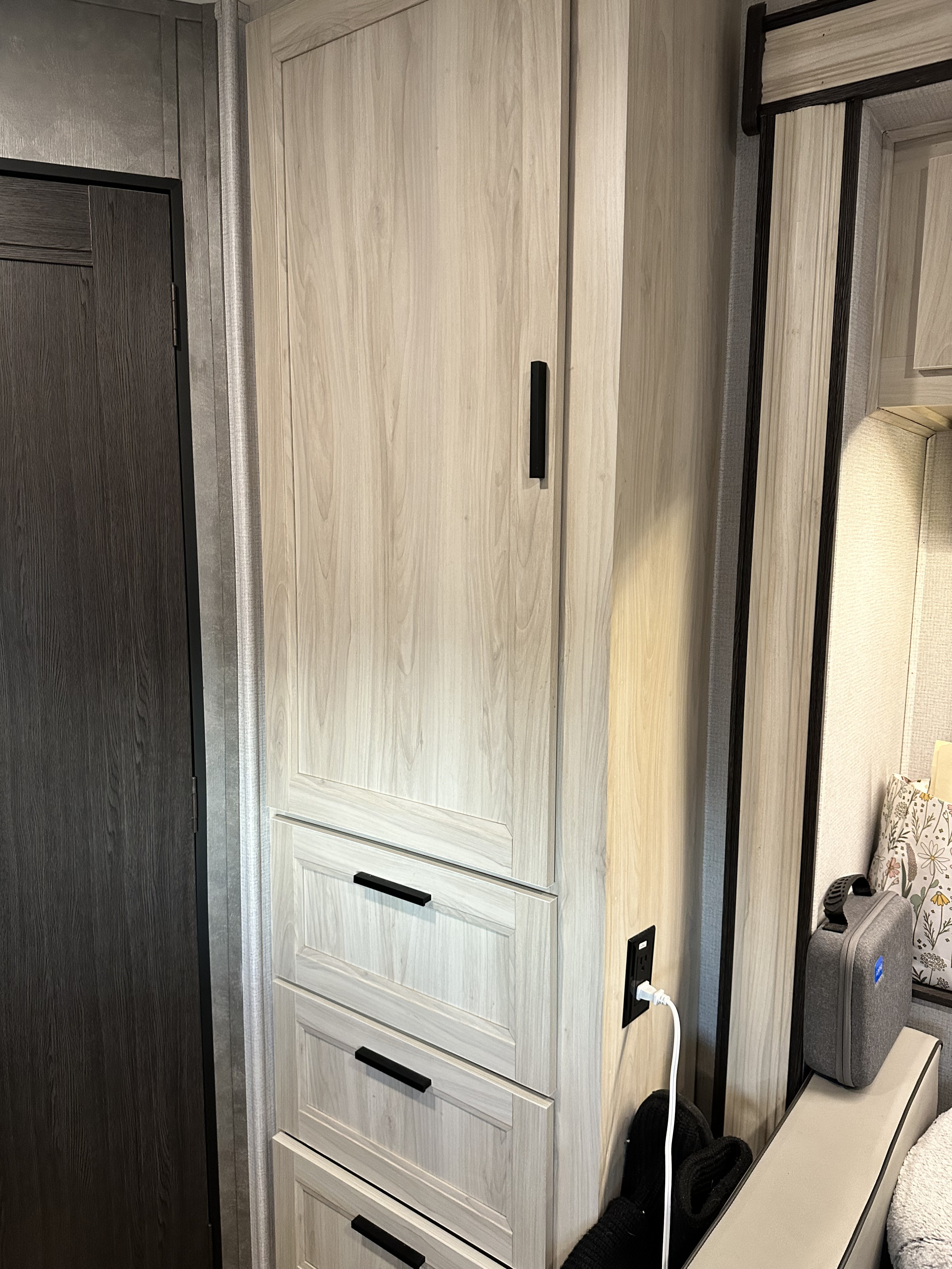 RV rental bedroom storage with light wood cabinetry, multiple drawers, a dark door, and a convenient power outlet.. Forest River 2551 dsle 2021