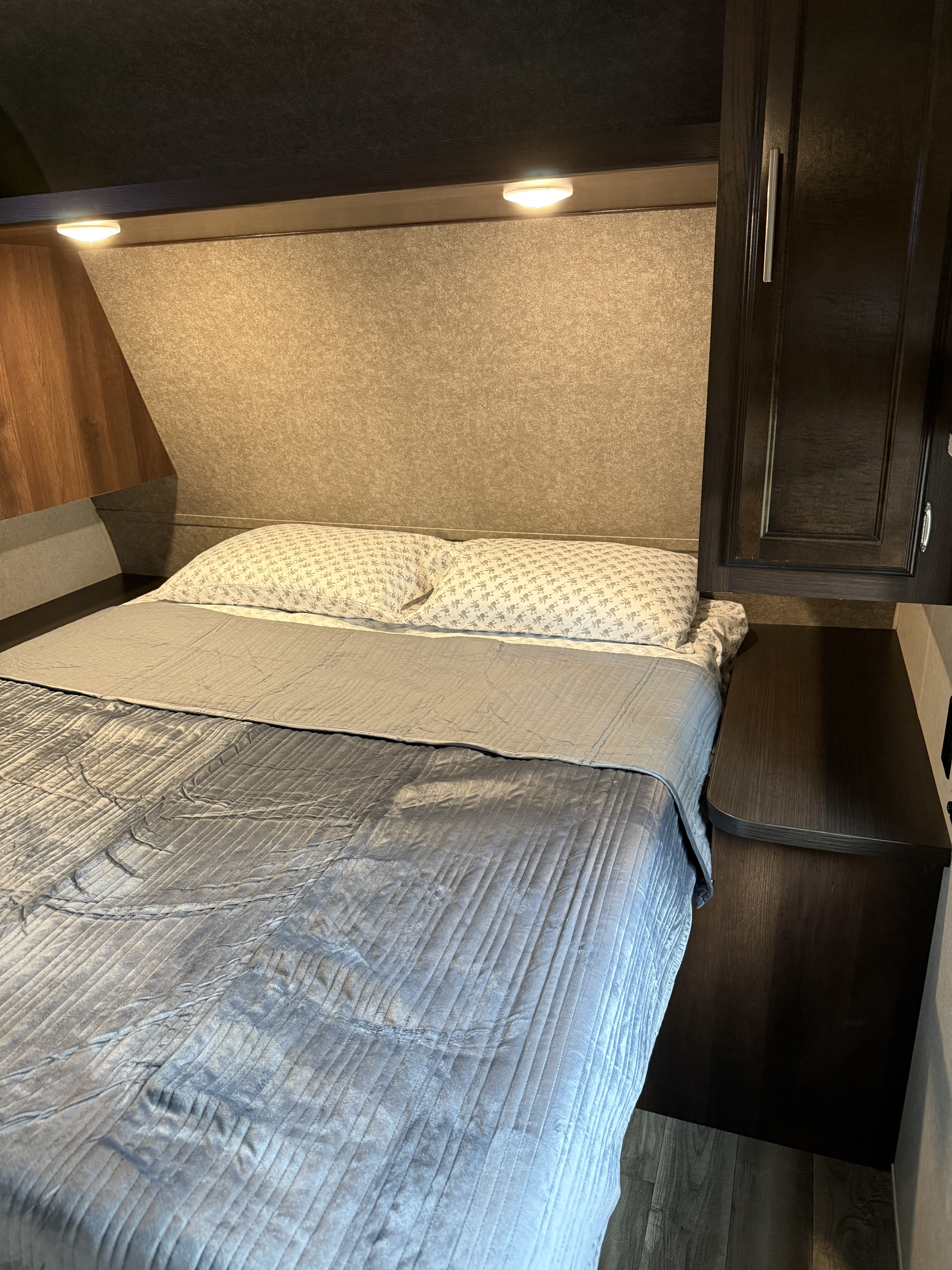 RV rental bedroom with a comfortable bed, warm overhead lighting, and integrated dark wood storage and nightstand.. Jayco Jay Flight SLX 2019