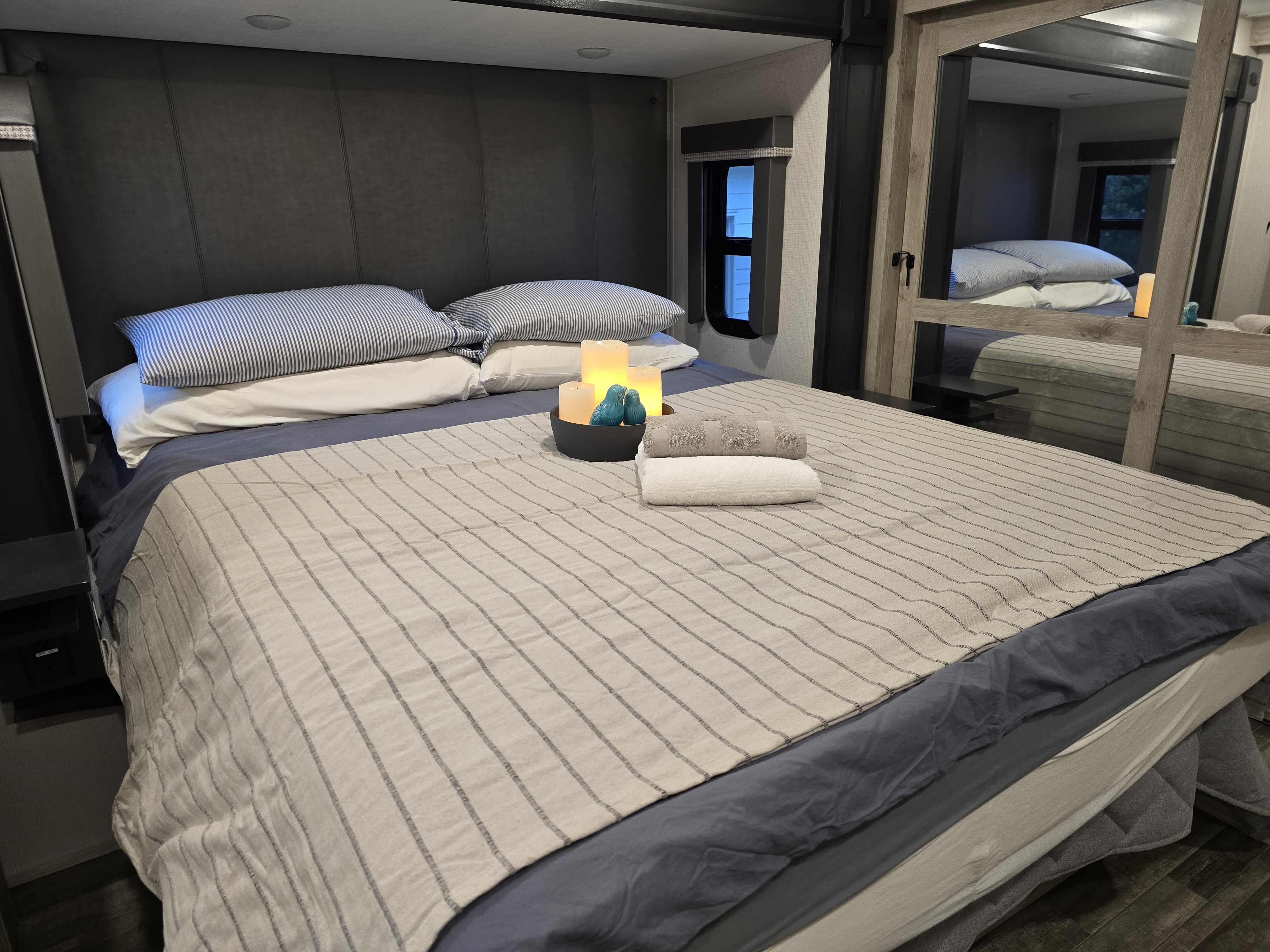 This RV rental offers a comfy bedroom with striped bedding, glowing candles, and plush towels for your relaxation.. Keystone RV Avalanche 2023