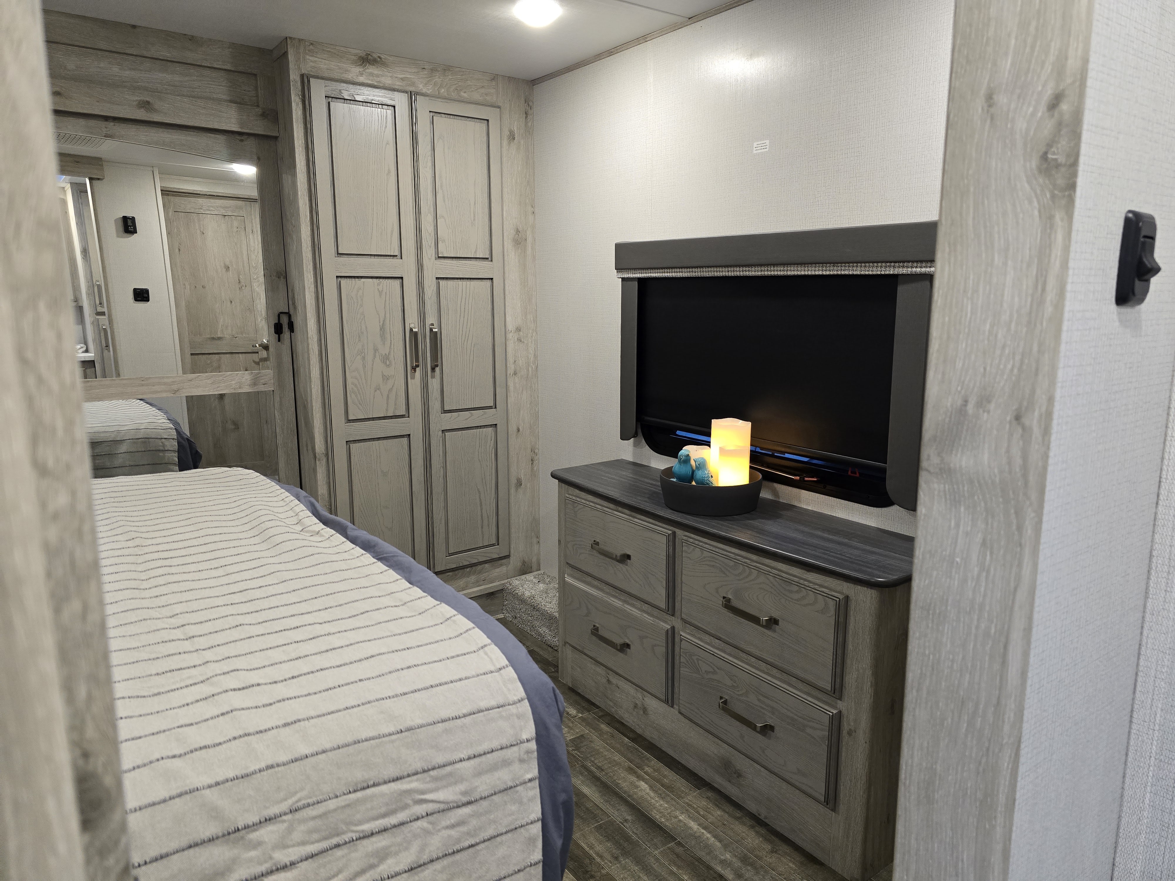 RV rental bedroom: striped bed, wood-look closet & dresser with TV. A compact, well-appointed interior space.. Keystone RV Avalanche 2023