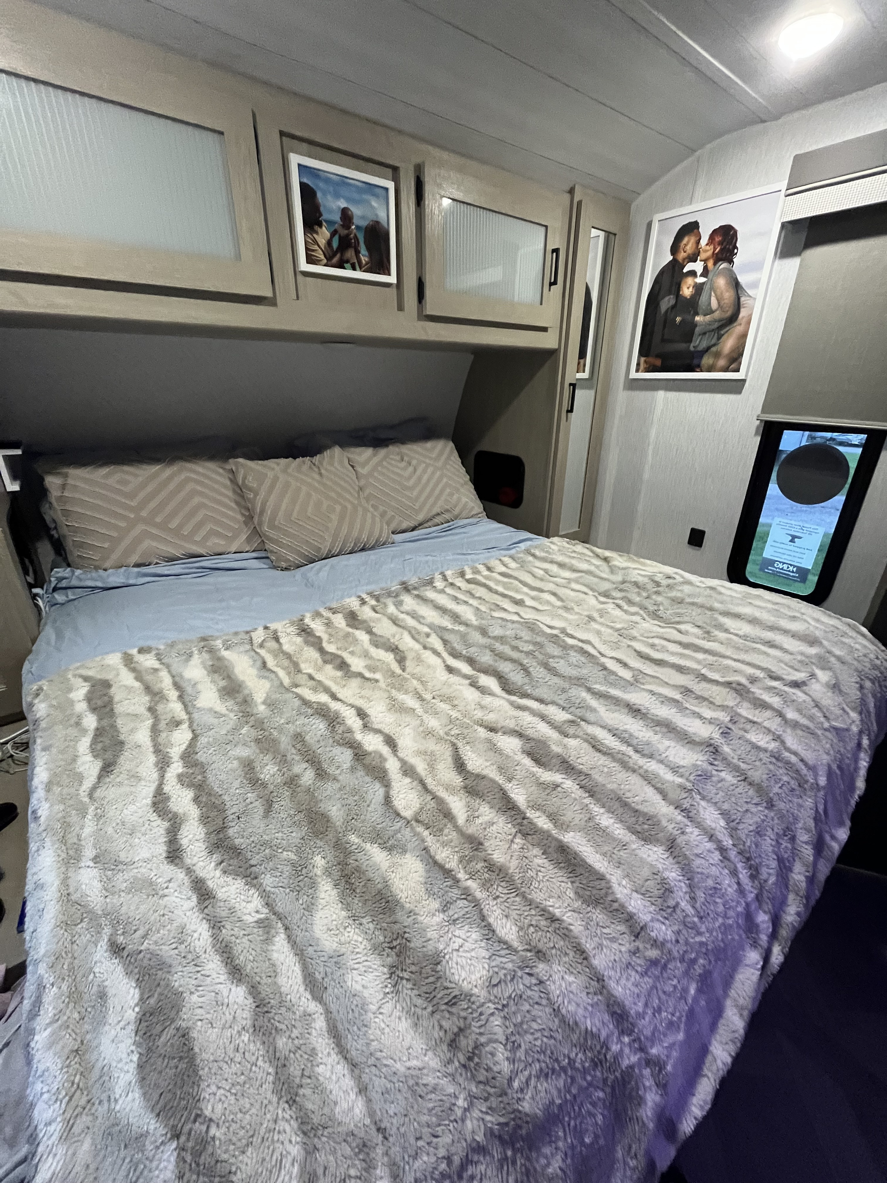 This cozy RV rental bedroom features a comfortable bed with a fuzzy blanket, overhead cabinets, and framed family photos.. Salem Forest River 2023