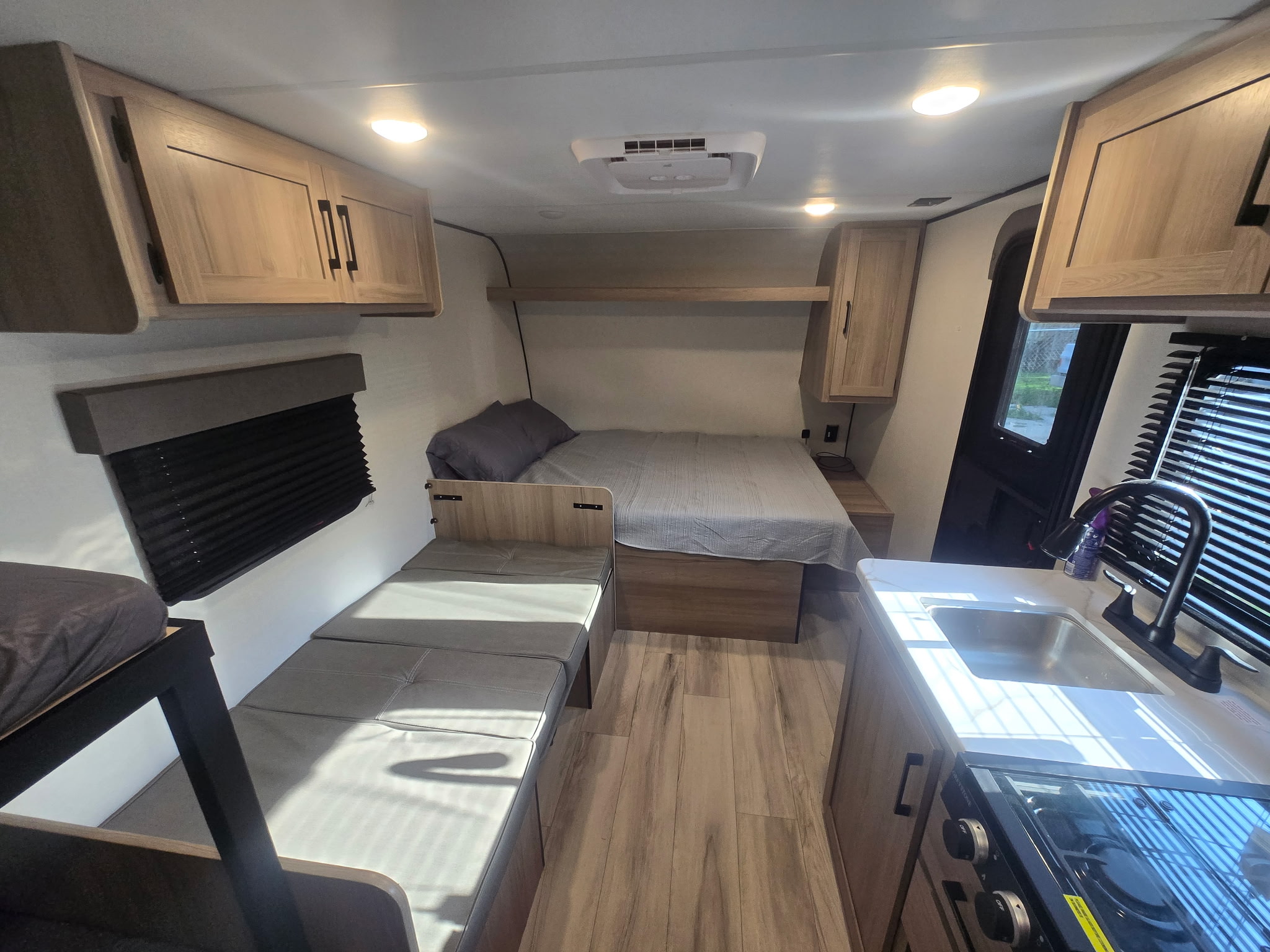 Clean RV rental interior featuring a bedroom area with a main bed and bunk beds, plus a compact kitchenette.. Keystone Colman 2025