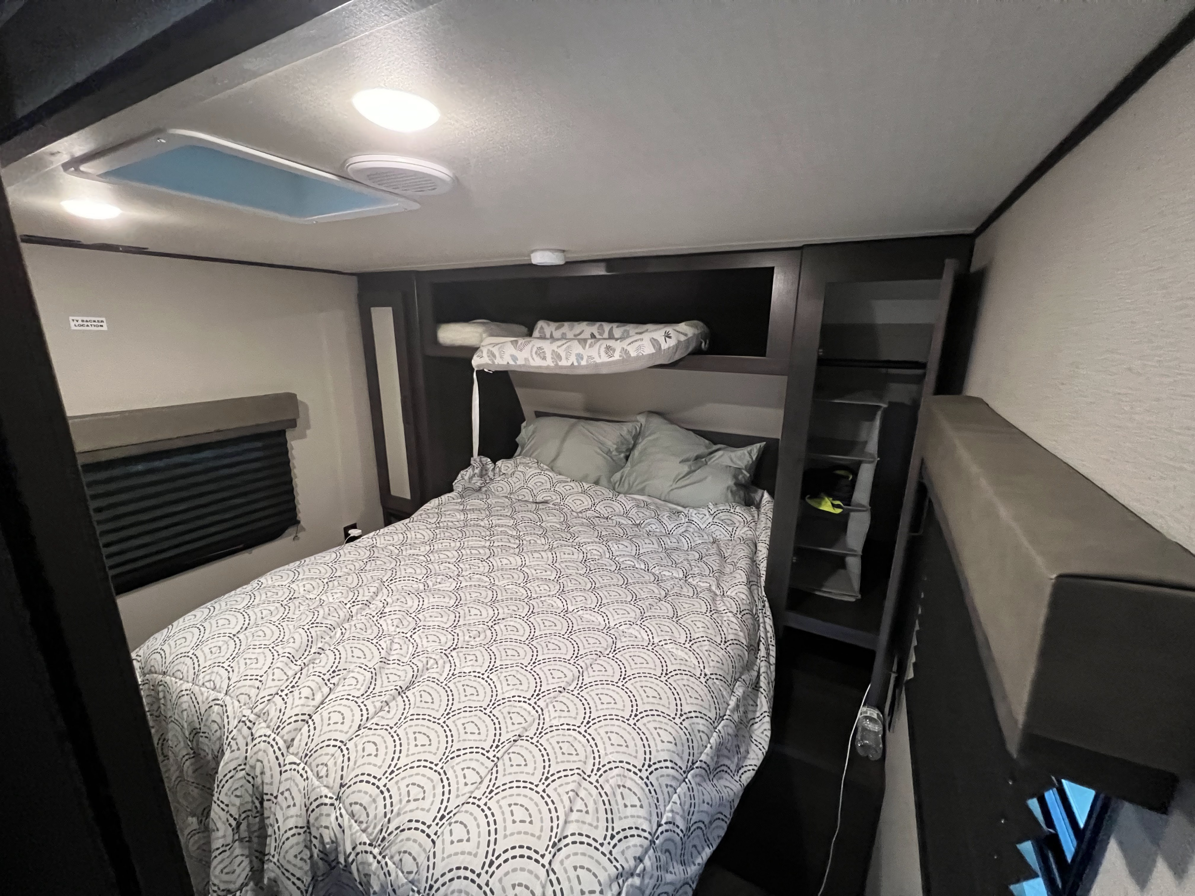 RV rental's cozy bedroom: main bed, upper bunk, window with blind, and built-in storage shelves.. Grand Design Transcend Xplor 2022