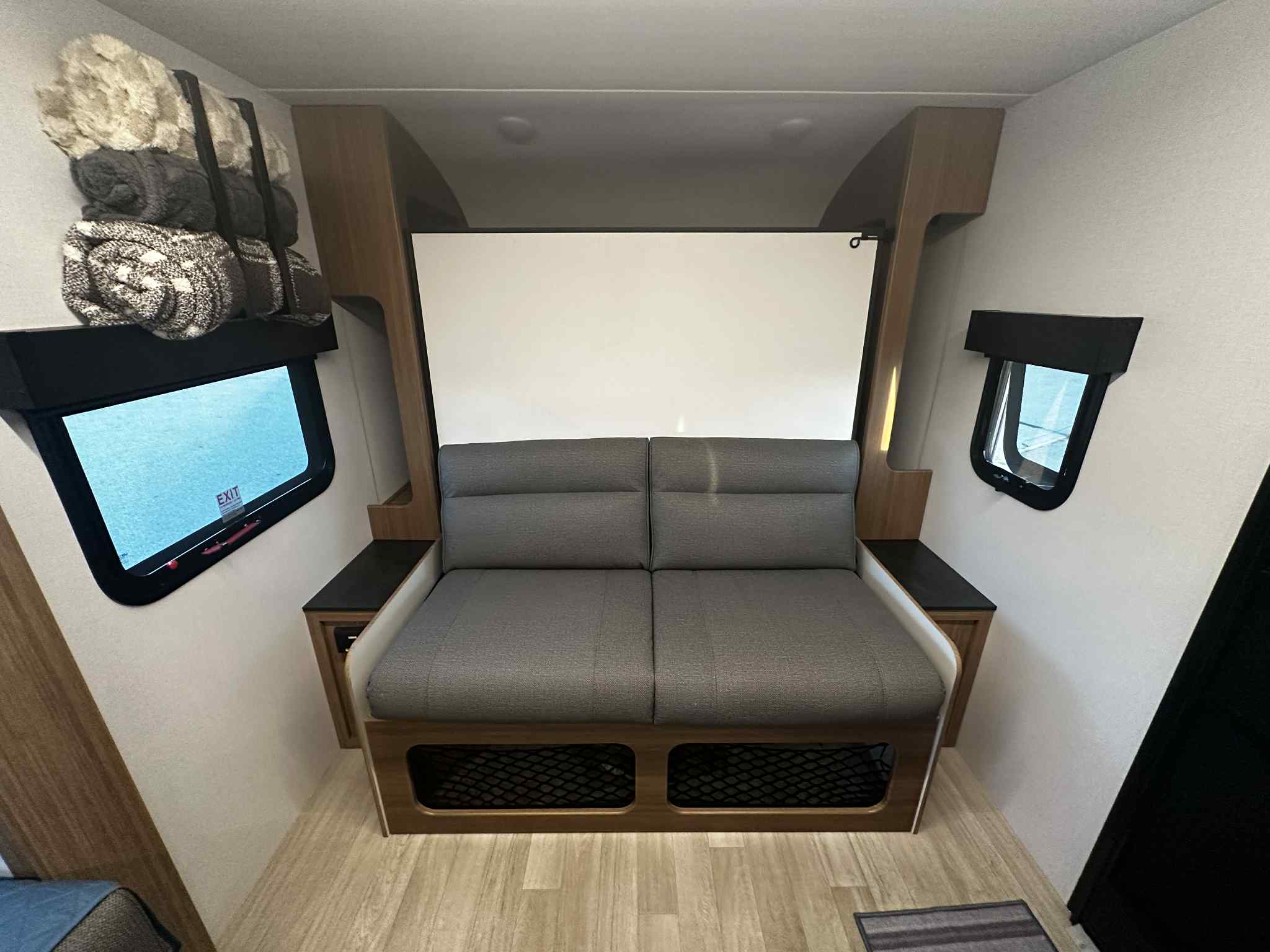 This RV rental offers a versatile interior with a gray convertible sofa, side windows, and overhead blanket storage.. Keystone RV Reign 18RB 2025