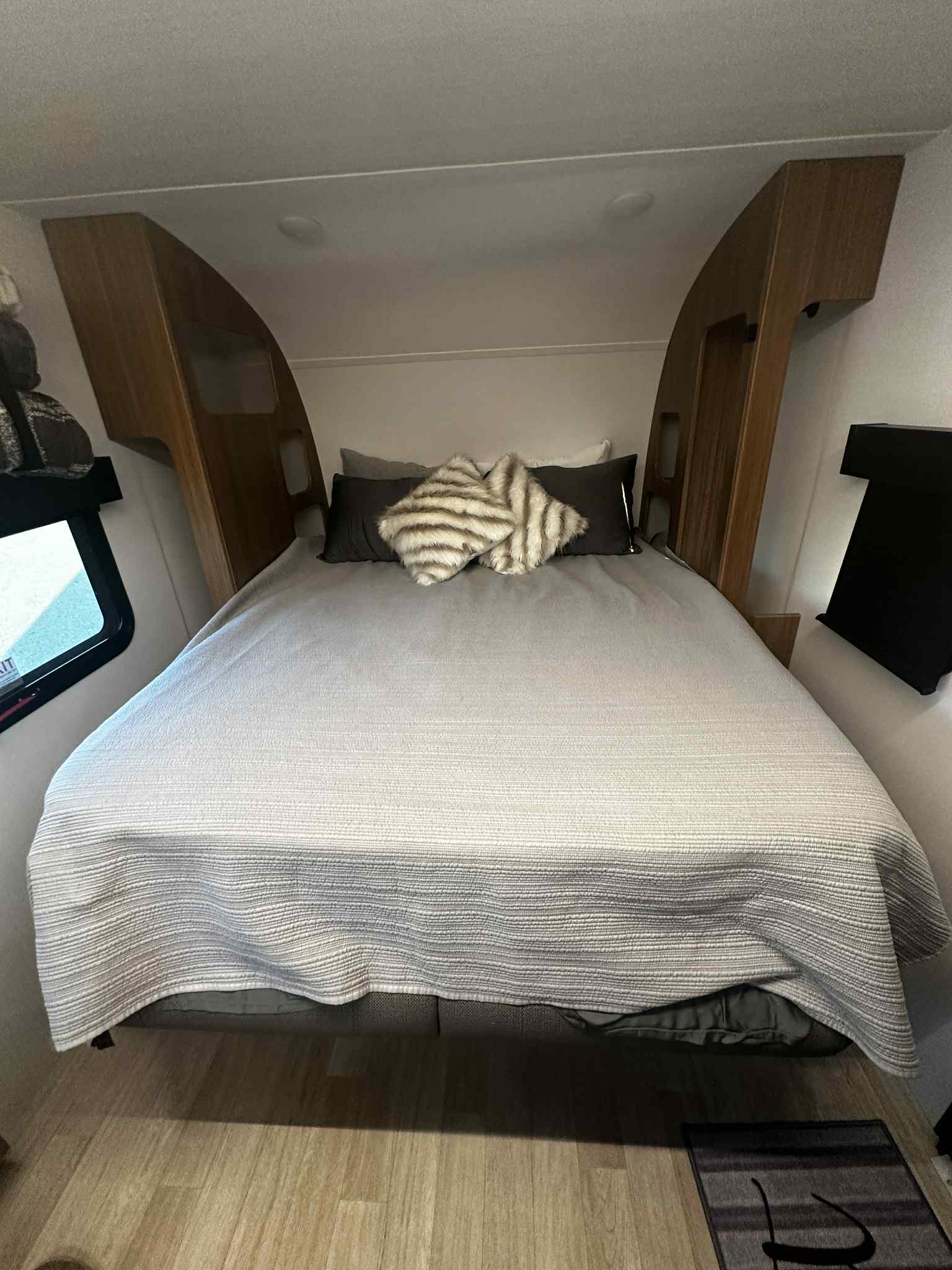 Interior of an RV rental: a neat bedroom with a spacious bed, light grey comforter, wood cabinetry, and window.. Keystone RV Reign 18RB 2025