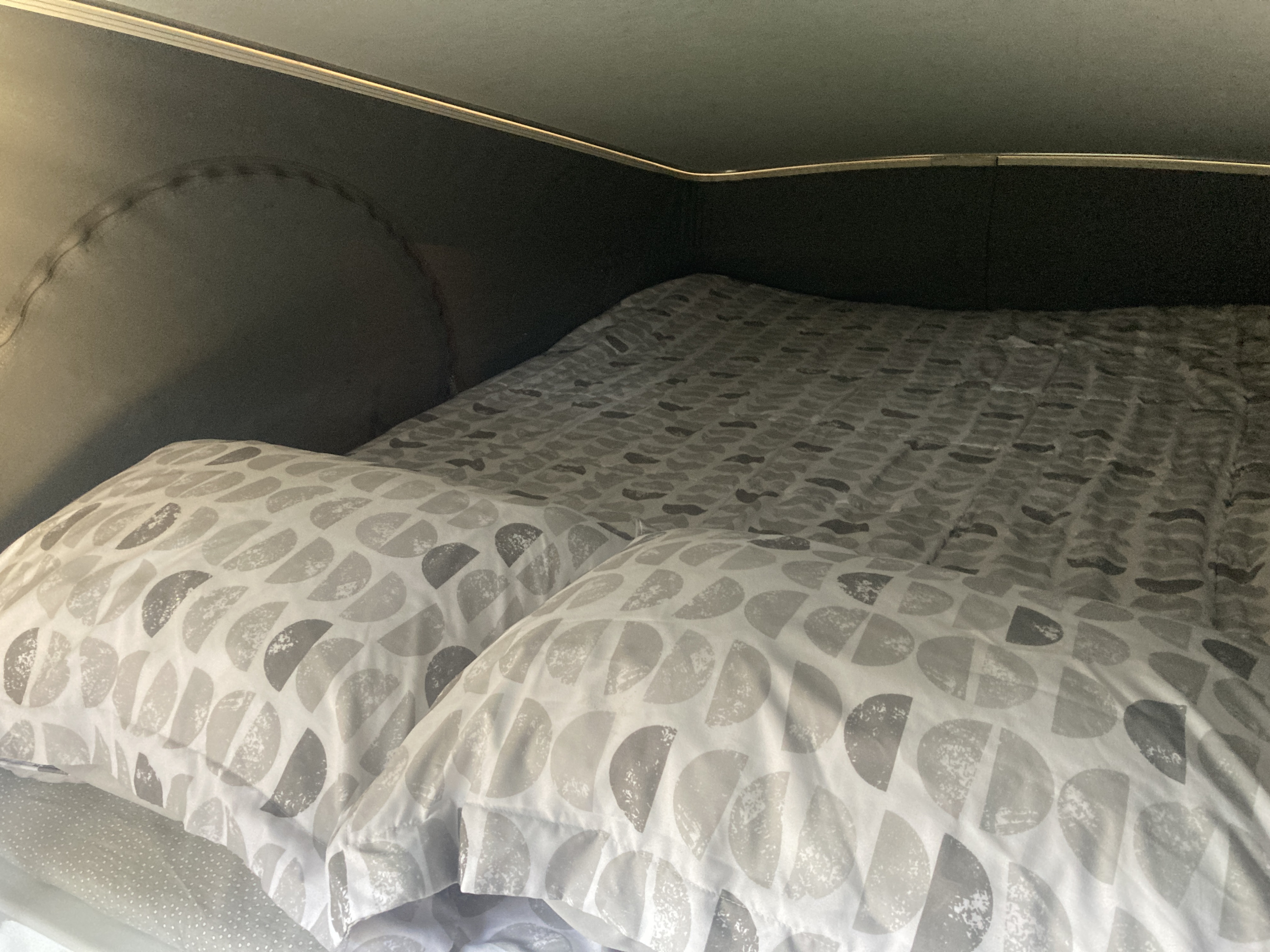 Cozy bed inside an RV rental, featuring soft grey patterned bedding and pillows, offering a comfortable sleeping area.. Winnebago Solis 2023