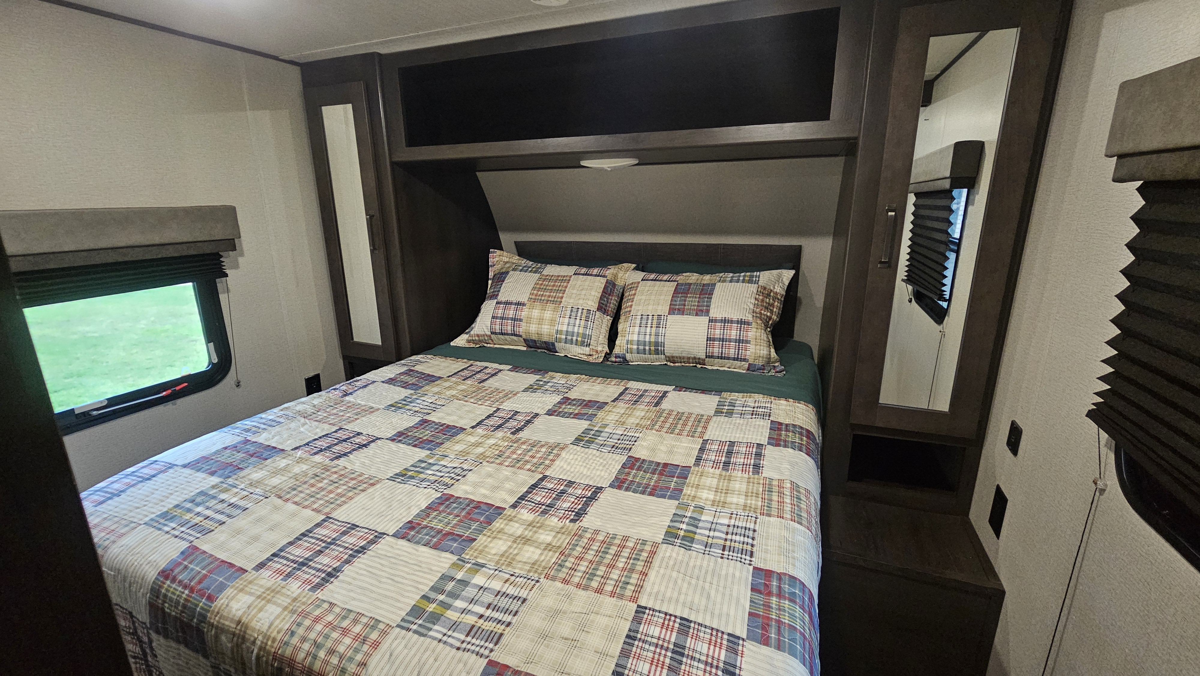 Experience comfort in this cozy RV rental bedroom. Features a patchwork bedspread, ample storage, and a scenic window view.. Grand Design Transcend Xplor 2020