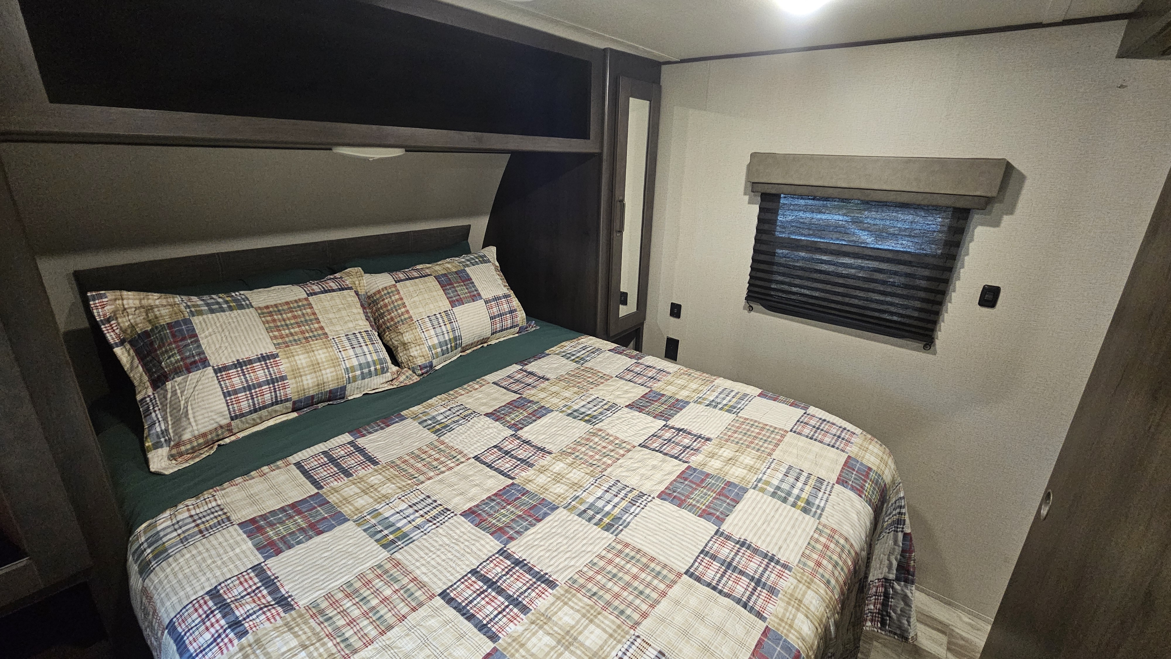 Cozy RV rental bedroom with patchwork bedding, overhead storage, and window. Perfect for your next trip!. Grand Design Transcend Xplor 2020