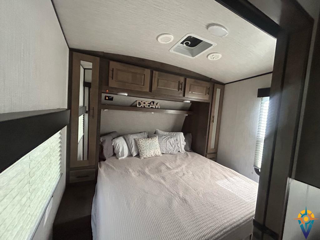 Inside an RV rental, a well-appointed bedroom with a large bed, "DREAM" sign, built-in cabinets, and window offers comfort.. Heartland Torque 2021