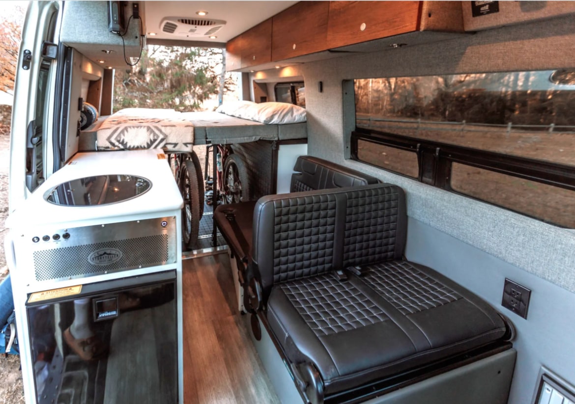 Interior of a modern rv rental camper van, featuring a bed, kitchen, seating area, and clever bike storage.. Storyteller Overland Storyteller Overland Class B 2021