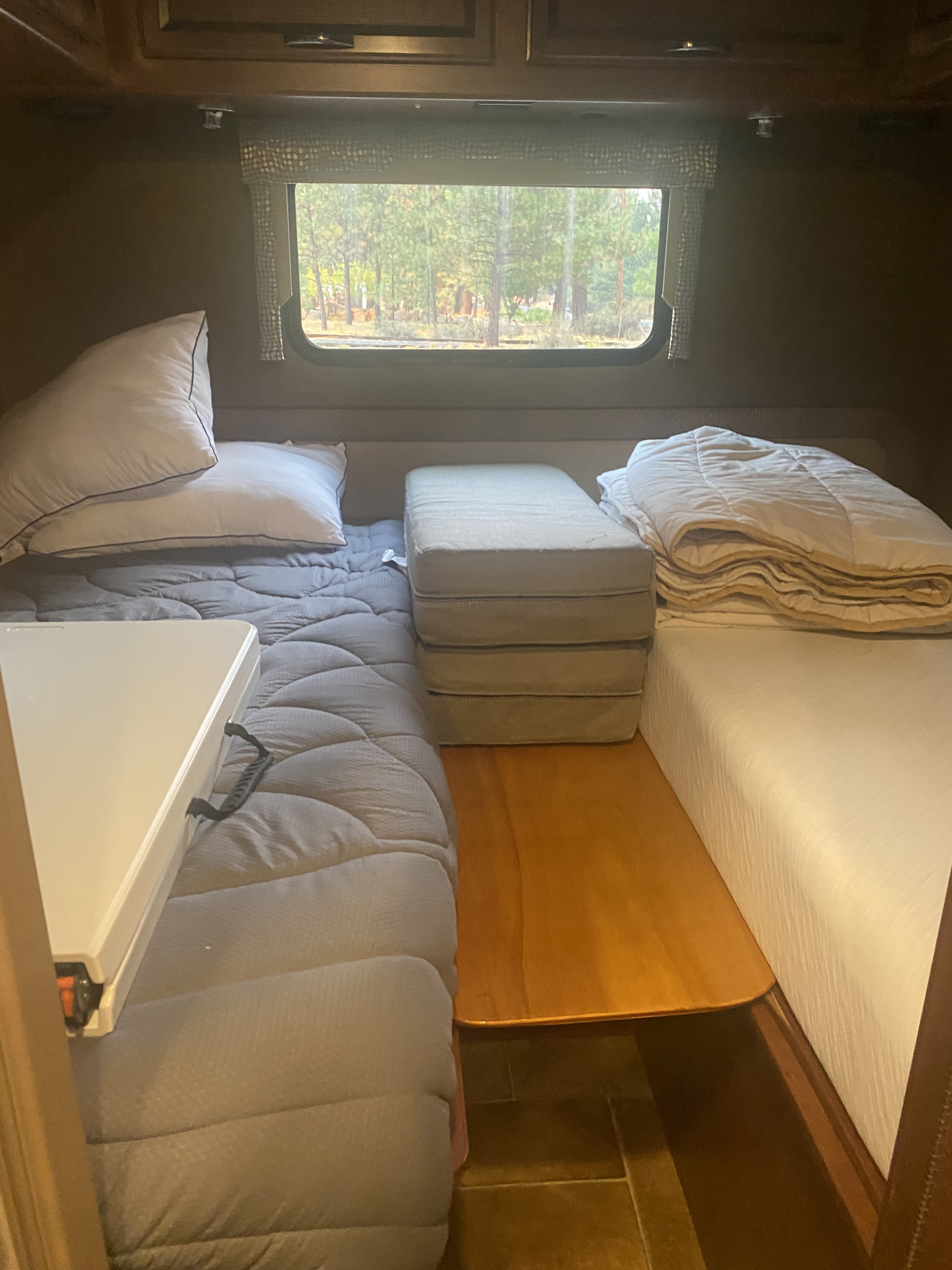 Cozy RV rental sleeping area: two beds, stacked cushions, and a window view of trees.. Thor Vegas 2016