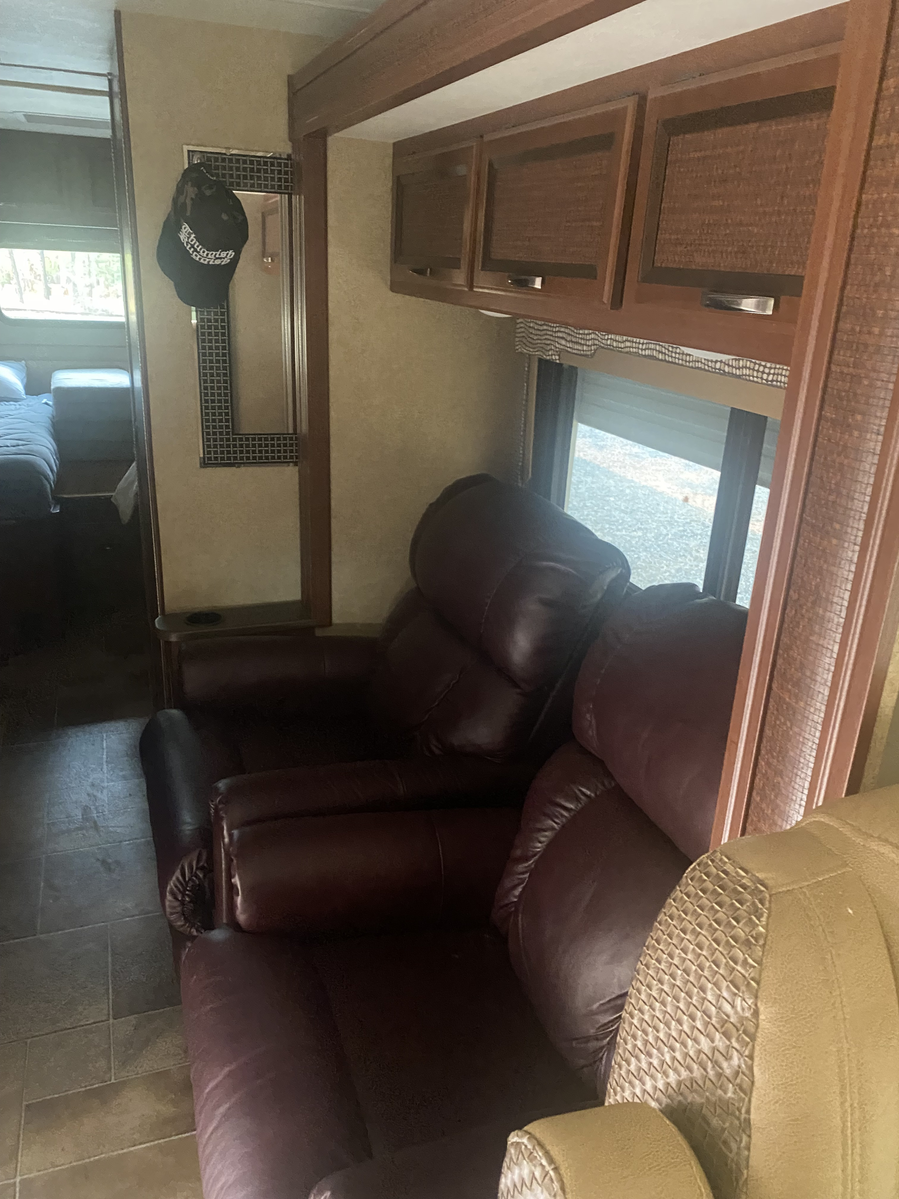View the comfortable interior of an RV rental, showing dark leather recliners, overhead cabinets, and a window view.. Thor Vegas 2016
