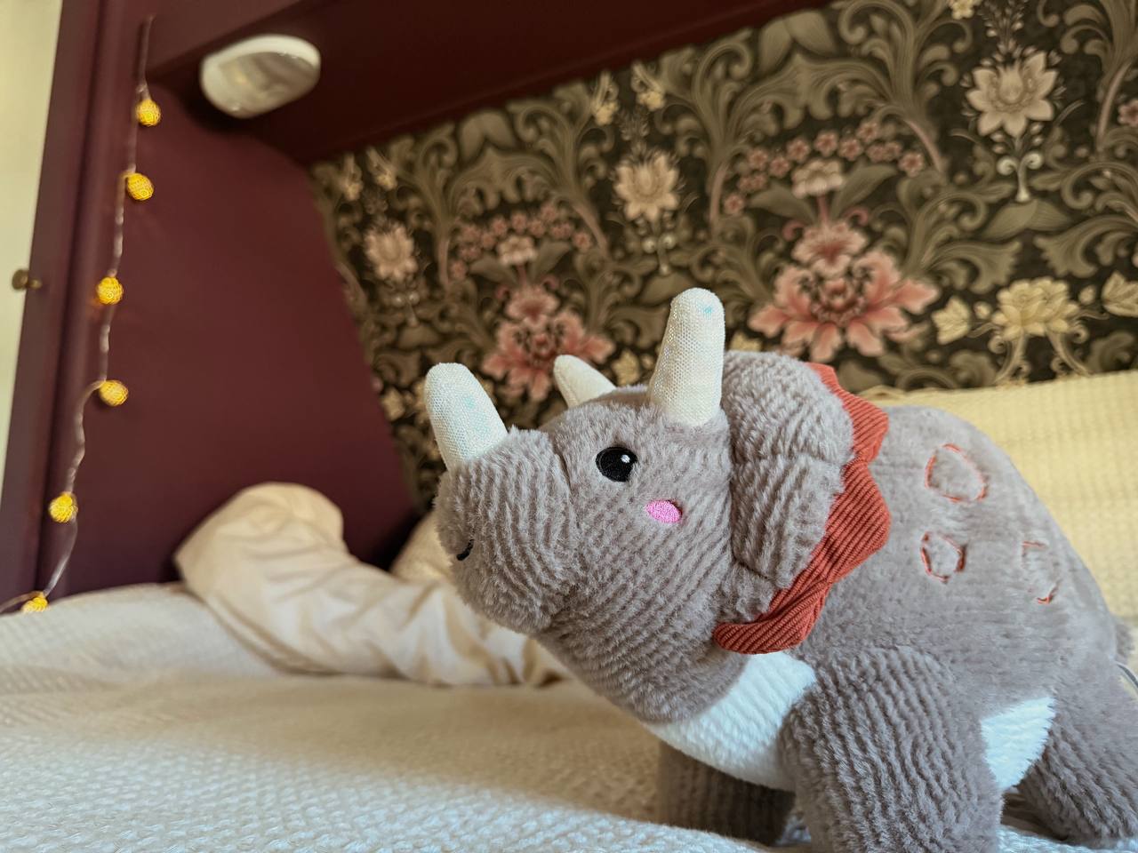 This plush triceratops toy enjoys a comfy bed in a cozy RV rental interior, lit by soft string lights.. Aspen Trail Aspen Trail Trailer 2016