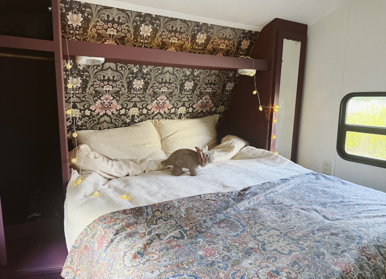 Inviting RV rental bedroom: floral wallpaper, soft bedding, a triceratops toy, and glowing string lights for a cozy stay.. Aspen Trail Aspen Trail Trailer 2016