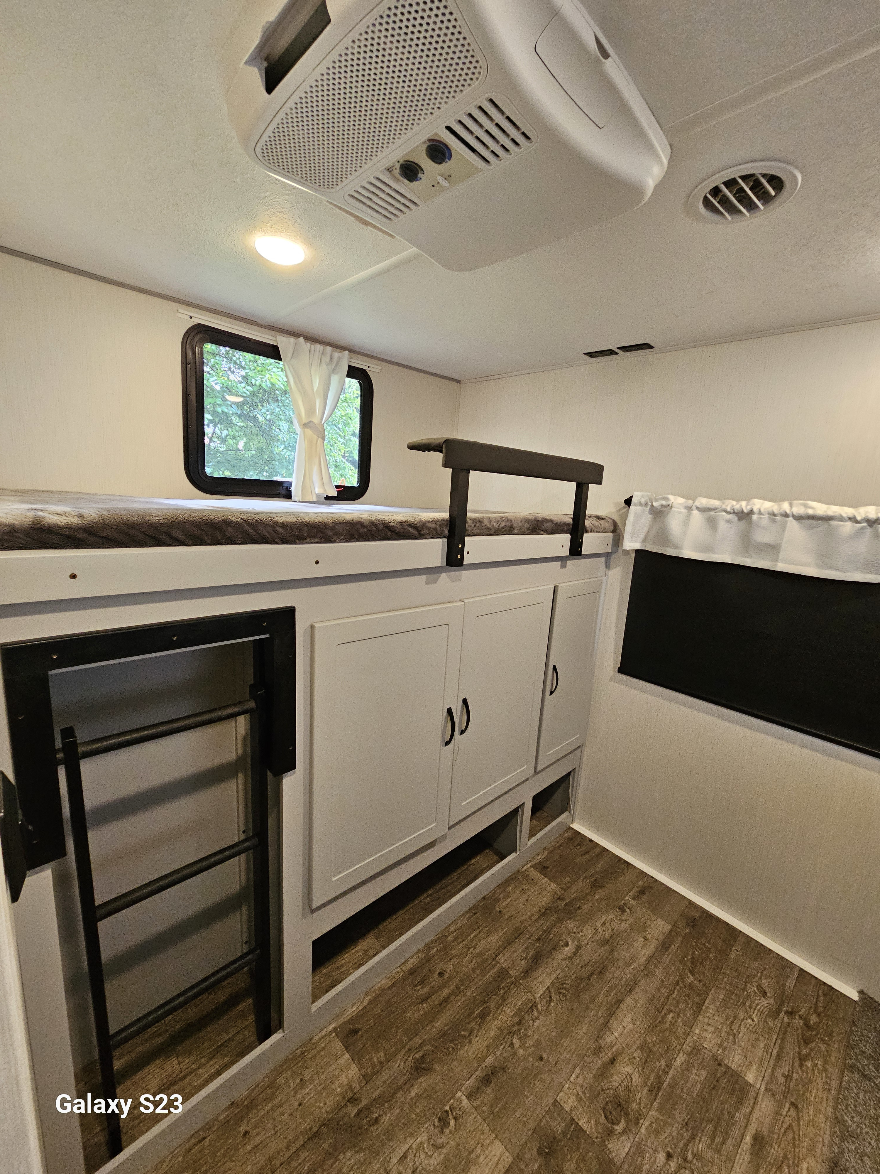 Interior of an **rv rental** showing a bunk bed with ladder, built-in cabinets, wood-look floor, and ceiling AC unit.. Forest River Vibe 2023
