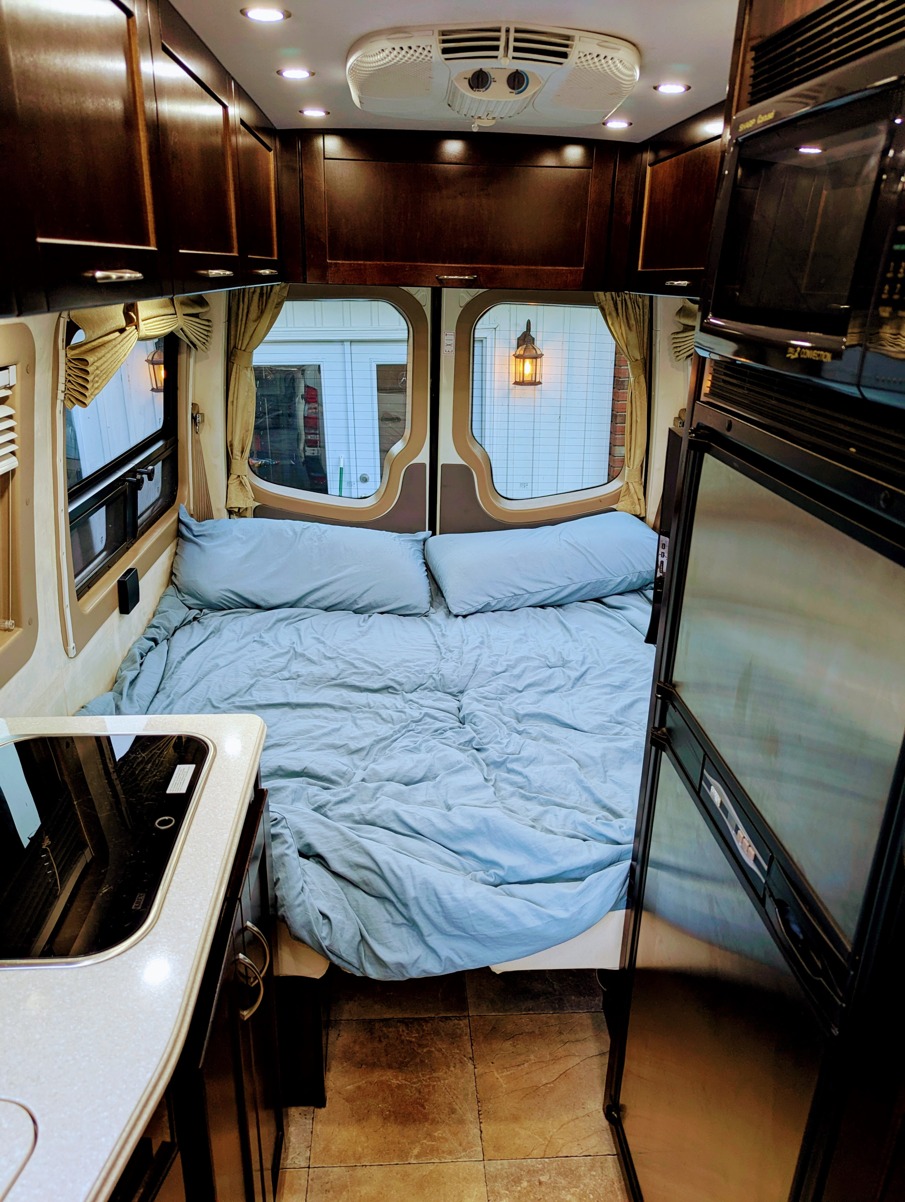 Inside a well-equipped rv rental: a light blue bed, dark wood cabinets, kitchenette, and fridge for comfortable travel.. Pleasure Way Plateau Ts 2013