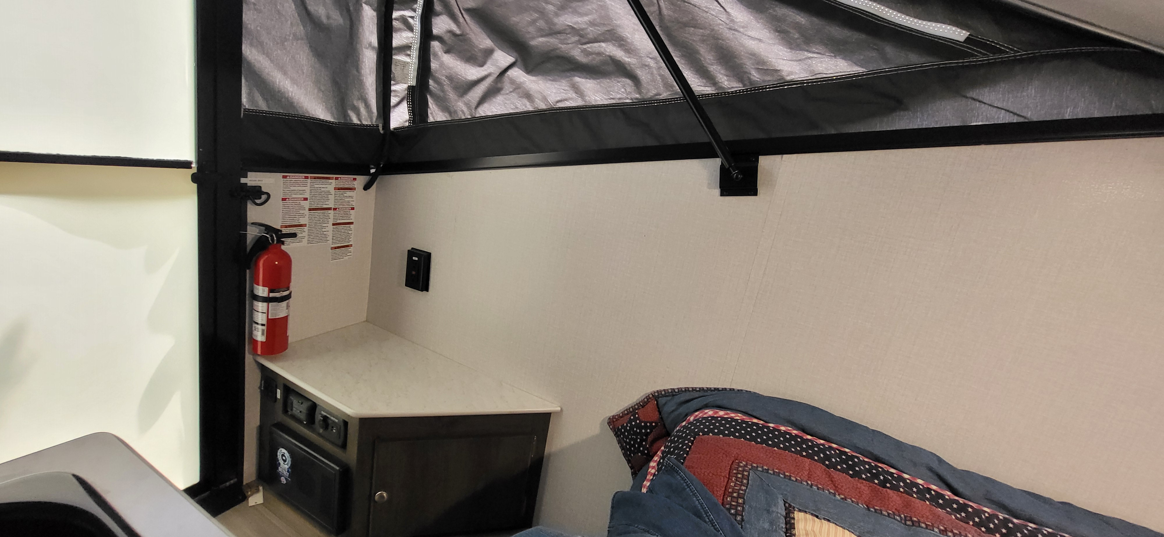 RV rental interior featuring a pop-up camper bed area, fire extinguisher, and a control panel on a compact cabinet.. Forest River Viking TD 2022