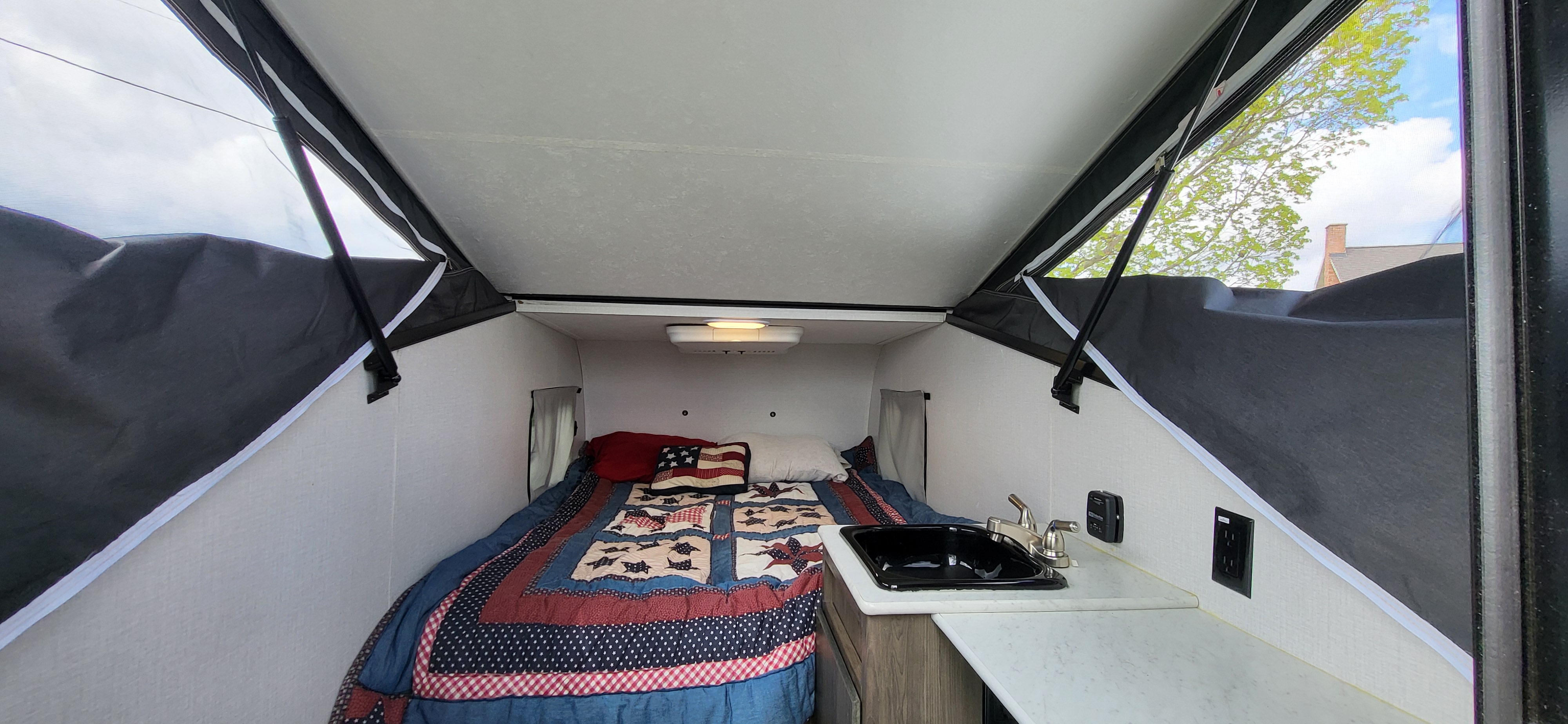 Cozy pop-up RV rental interior features a patriotic bed and small kitchen setup. Ideal for compact travel.. Forest River Viking TD 2022