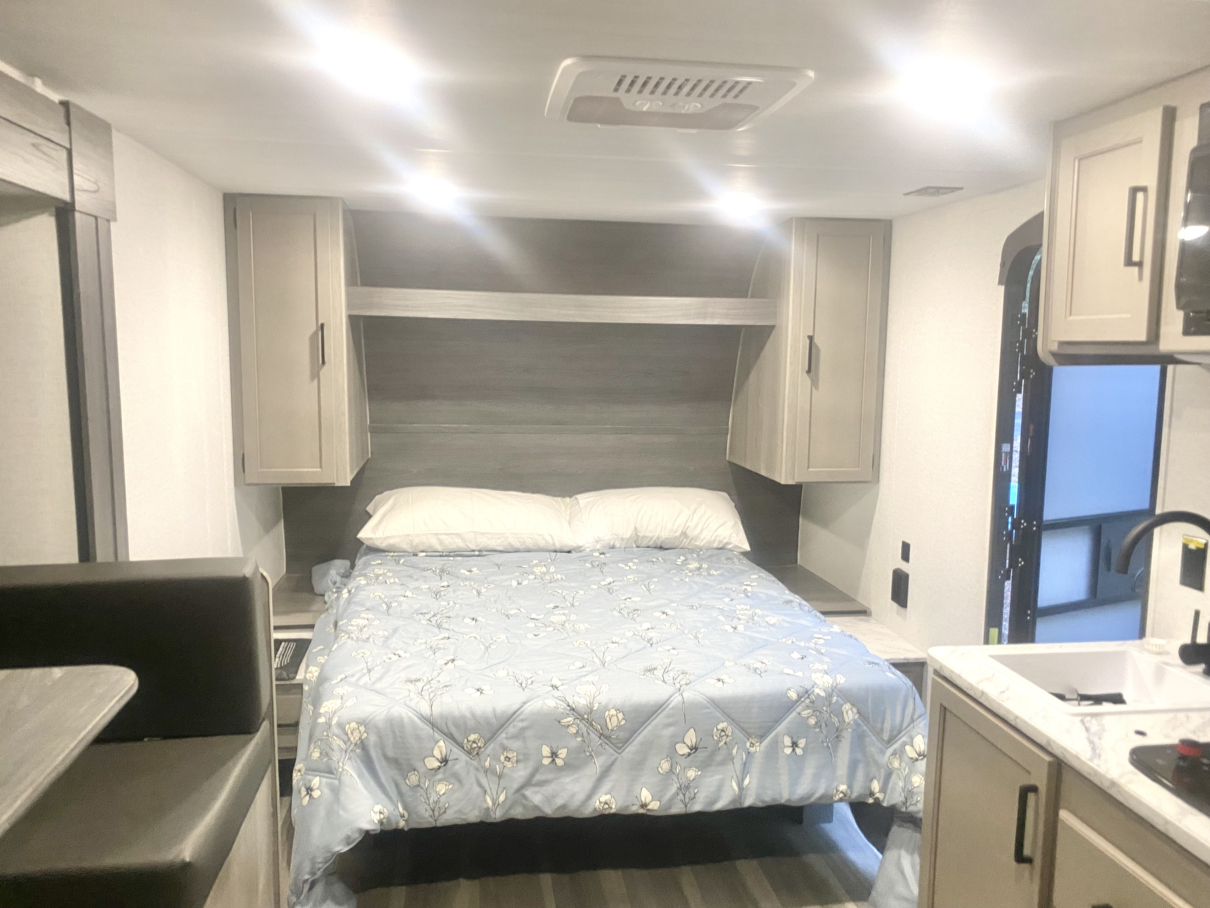 Cozy RV rental interior with a light blue floral bed, overhead storage, and integrated kitchen/dinette space.. Keystone RV Hideout Sport 2024