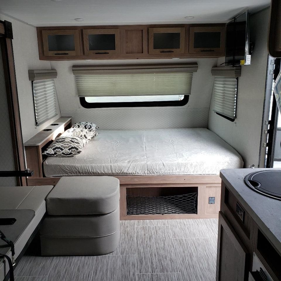 This RV rental showcases a cozy bedroom with overhead storage, compact kitchen, and seating area, perfect for travel comfort.. No Boundaries 19 2021