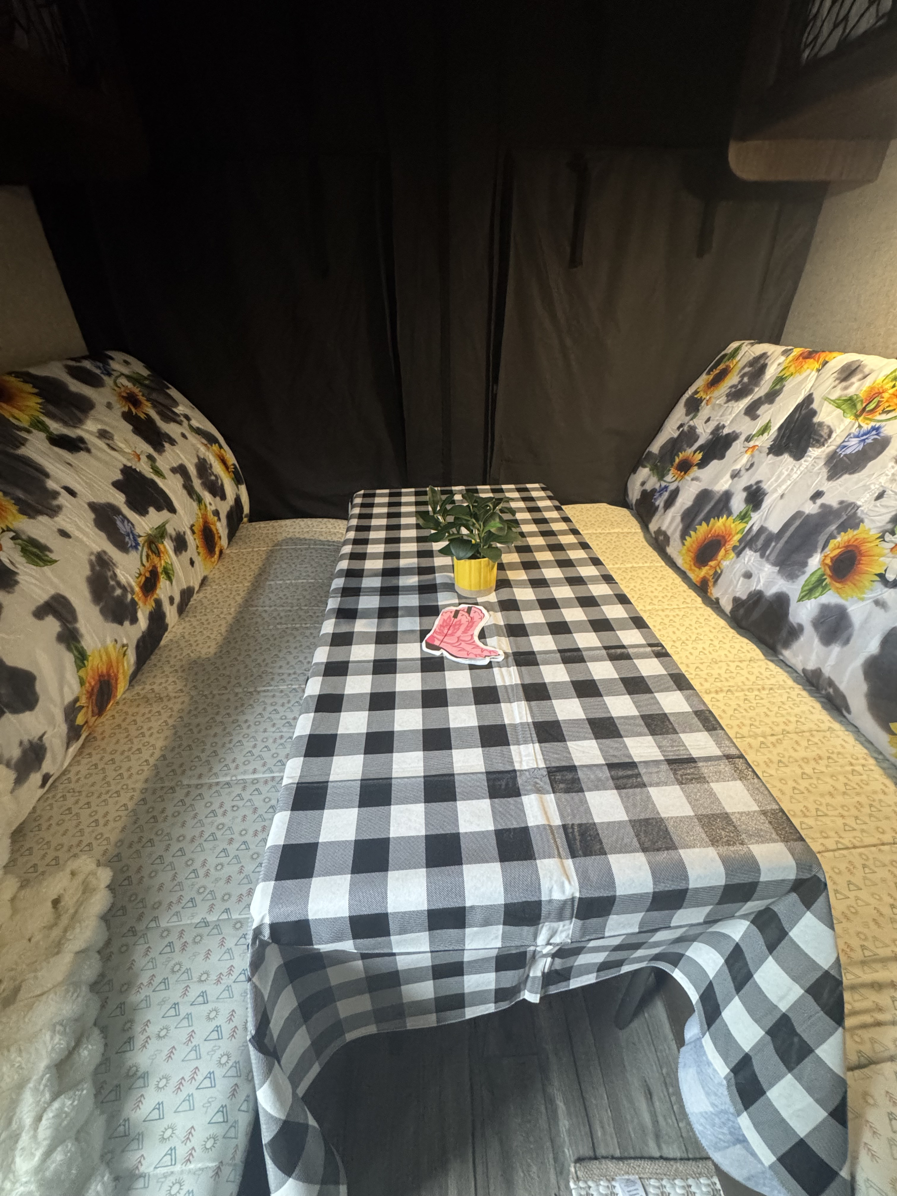 Cozy RV rental interior featuring sunflower and cow print beds, a black and white checkered table, and a small plant.. Forest River Cherokee Grey Wolf 2018