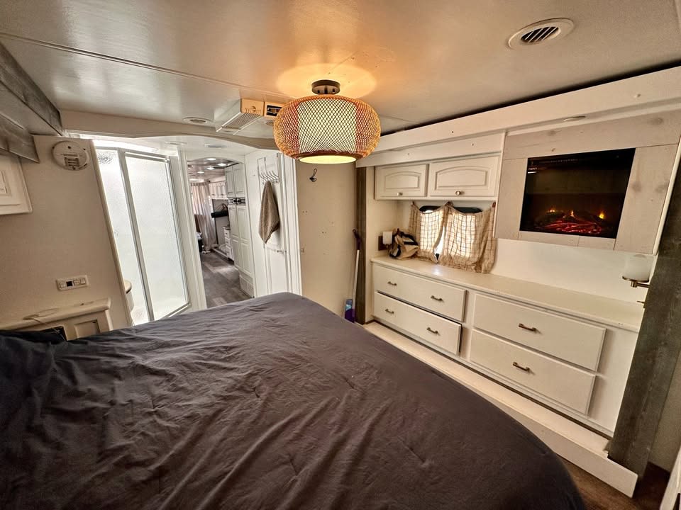 This inviting RV rental bedroom features a comfy bed, electric fireplace, white cabinets, and a shower stall.. Damon Corporation Tuscany 2008