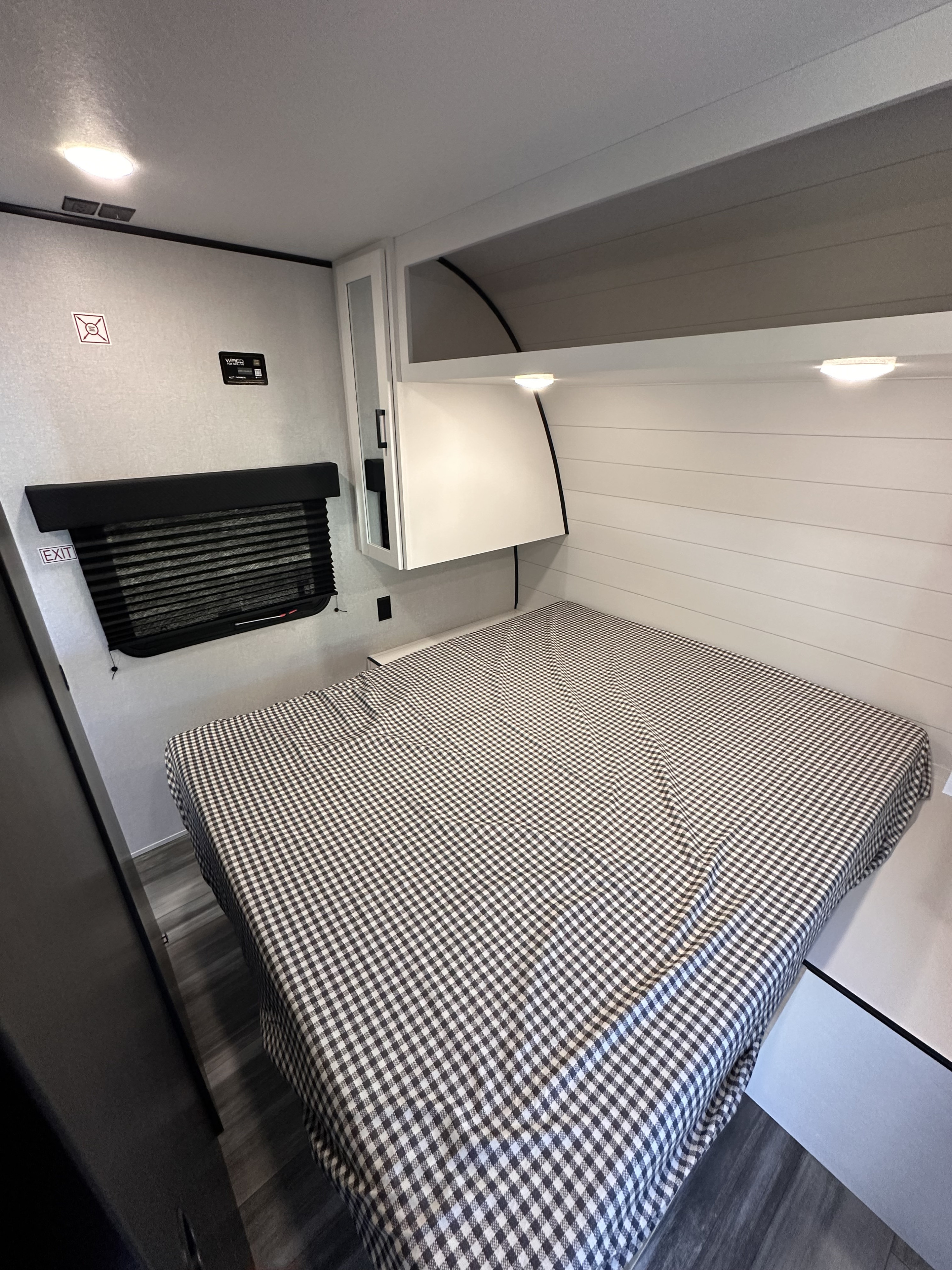 Inside a modern rv rental bedroom featuring a comfy checkered bed, compact storage, and shiplap-style walls. Ready for adventure.. Jayco Jay Flight 2026