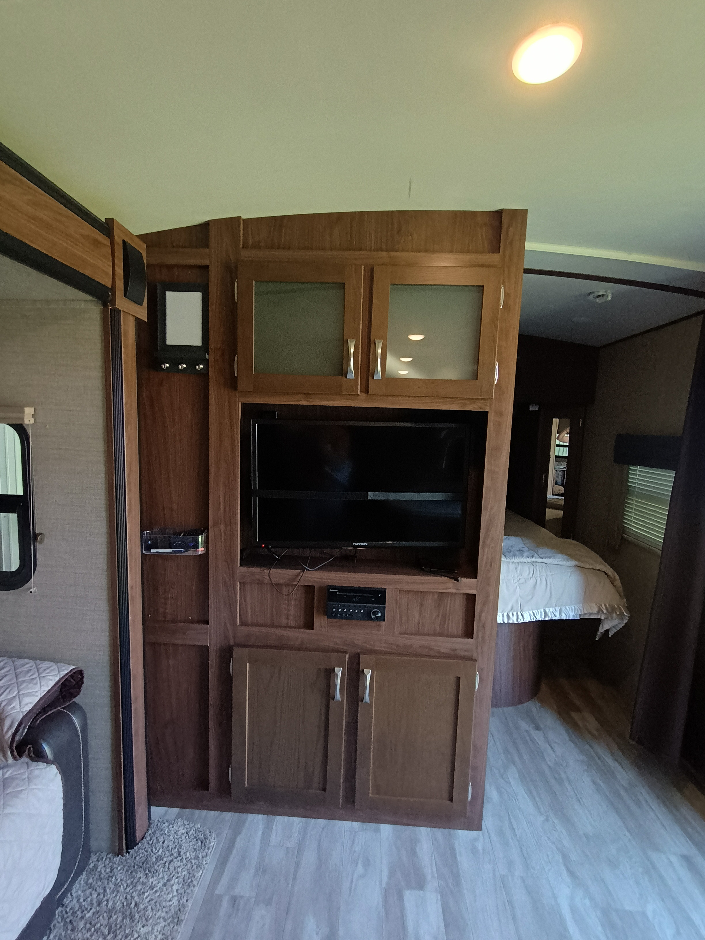 Spacious RV rental interior featuring a built-in wooden entertainment center with TV, storage, and light-colored flooring, looking towards the bedroom.. Dutchmen Aerolite 28dbhs 2017