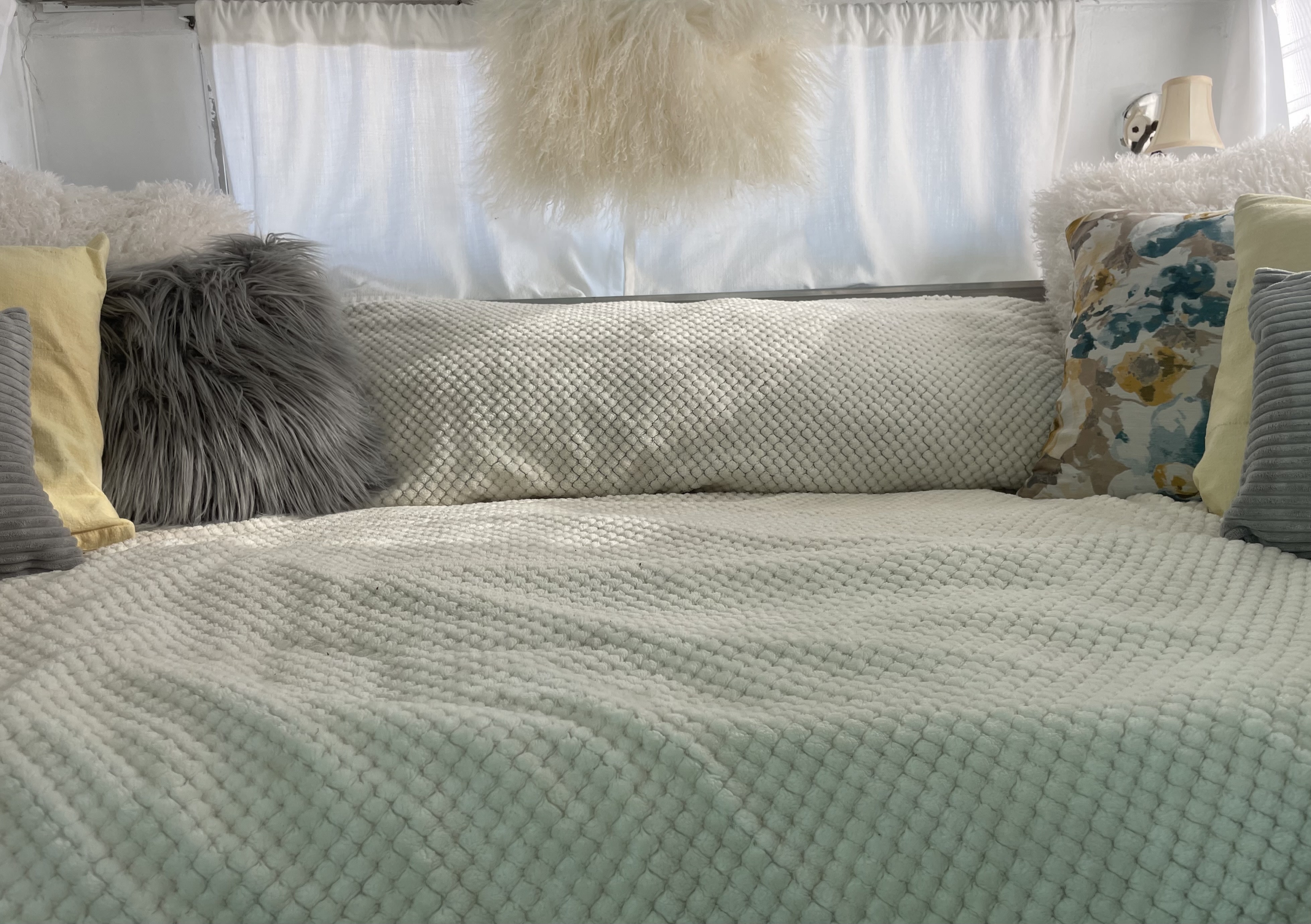 Cozy RV rental bed featuring textured white blankets, fluffy gray, white, and floral pillows.. Shasta Aristocrat 1969