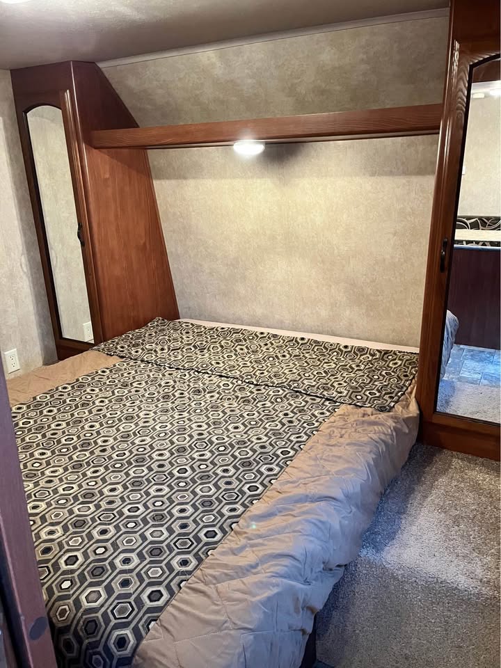 This RV rental bedroom features a comfy bed with patterned bedding, built-in wooden shelving, and mirrored accents.. Forest River Wildwood X-Lite 2013