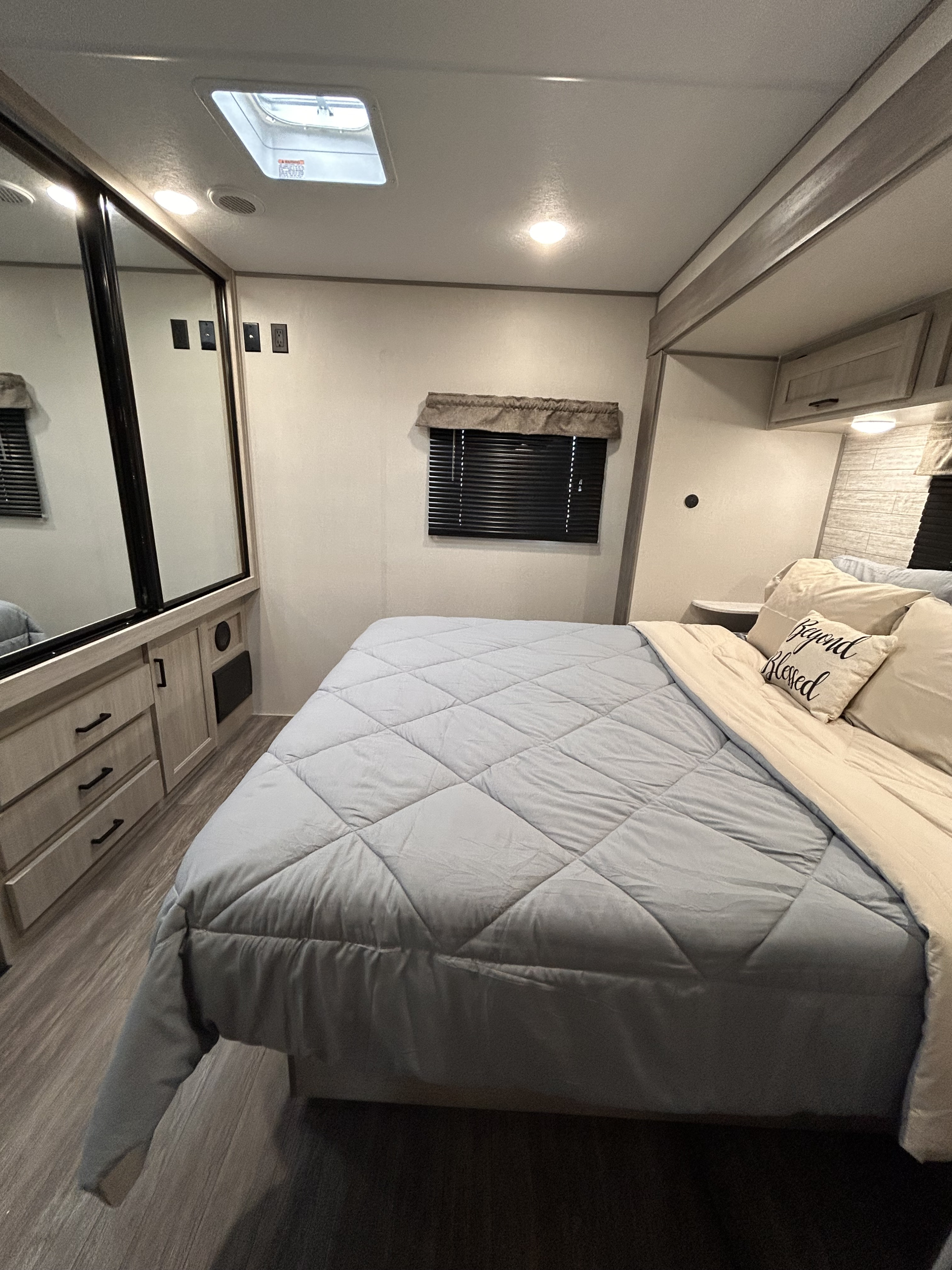 Inside a modern RV rental: a cozy bedroom with a quilted bed, mirrored closet, and ample storage for your journey.. Forest River 26FKDS 2025